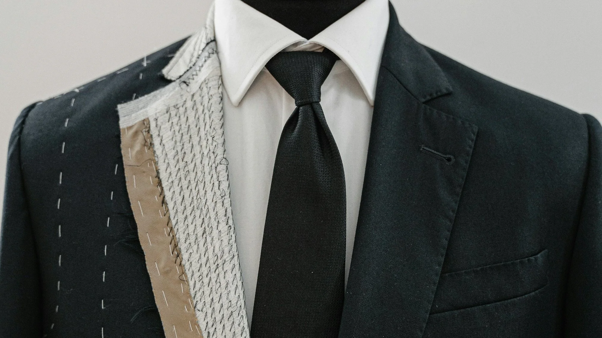Costume de tailleur noir avec une chemise blanche et une cravate noire, avec un entoila traditionnel visible sur le revers gauche.