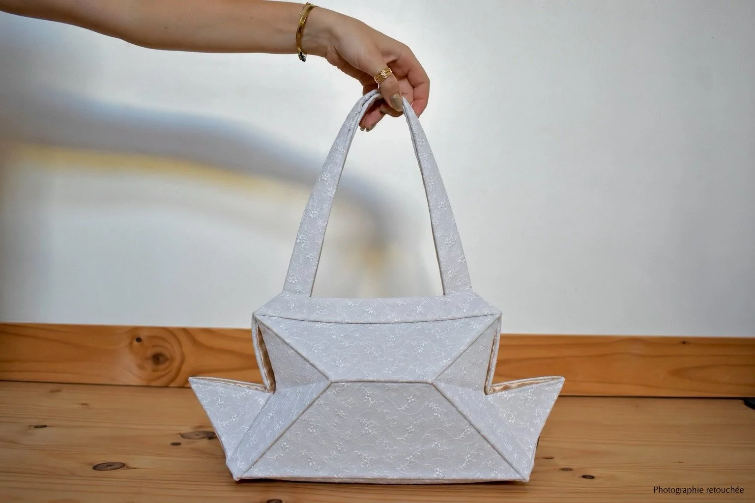 Une main tenant un sac blanc en forme de bateau ou de navire, posé sur une surface en bois, contre un fond neutre.