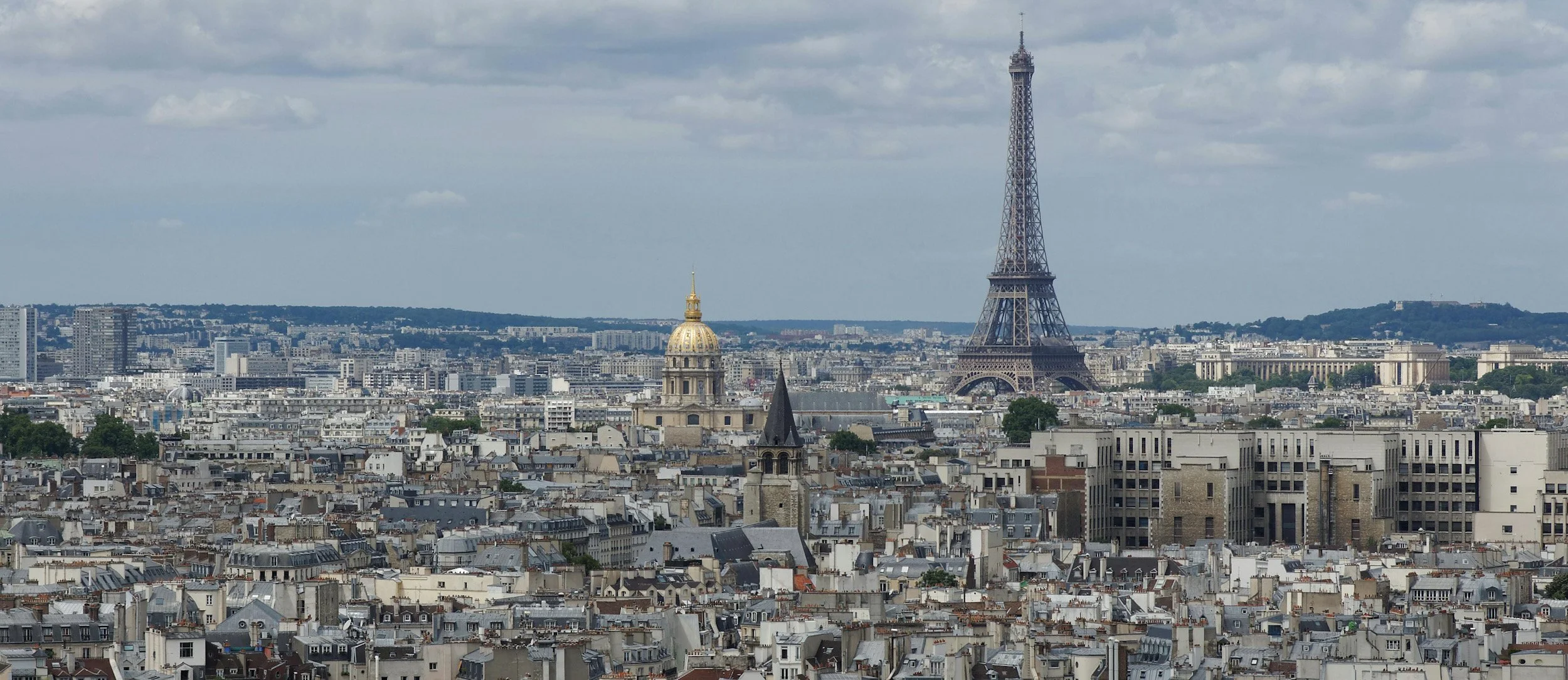 Vue de Paris avec la Tour Eiffel en arrière-plan, un dôme doré et des toits de bâtiments historiques.
