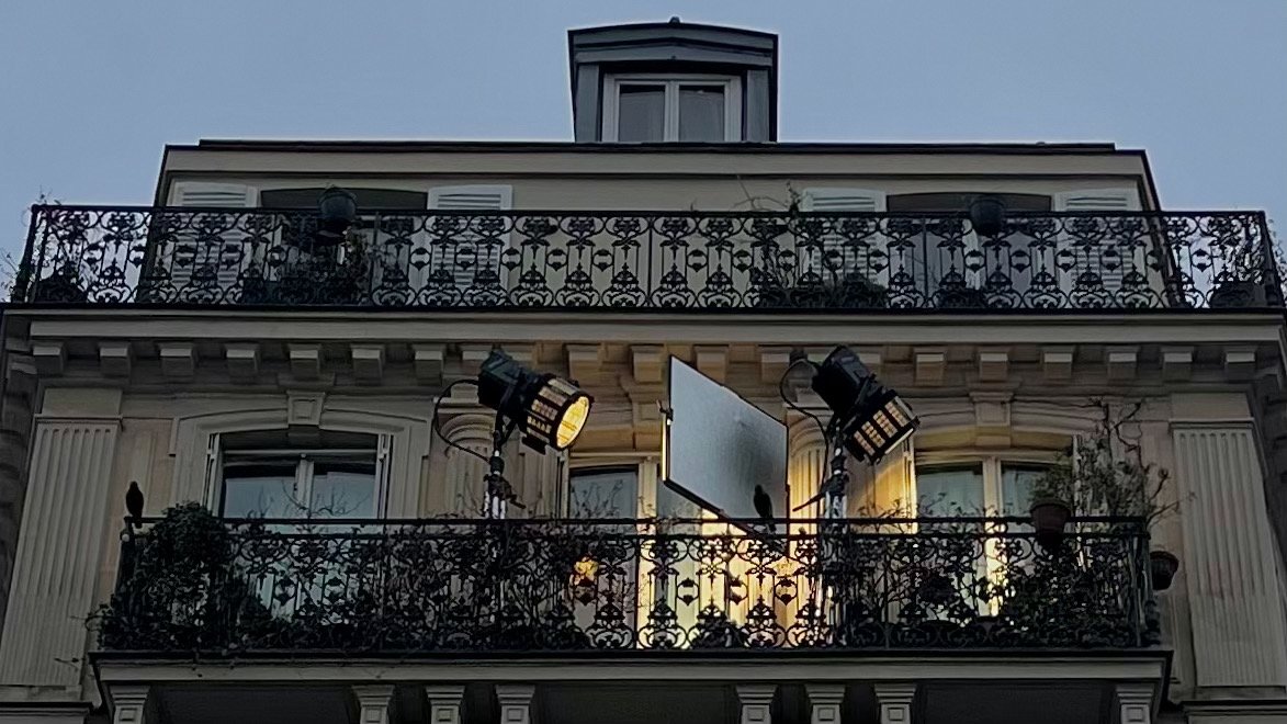 Balcon avec lampes de studio, écran blanc, et plantes sur la façade d'un immeuble haussmannien