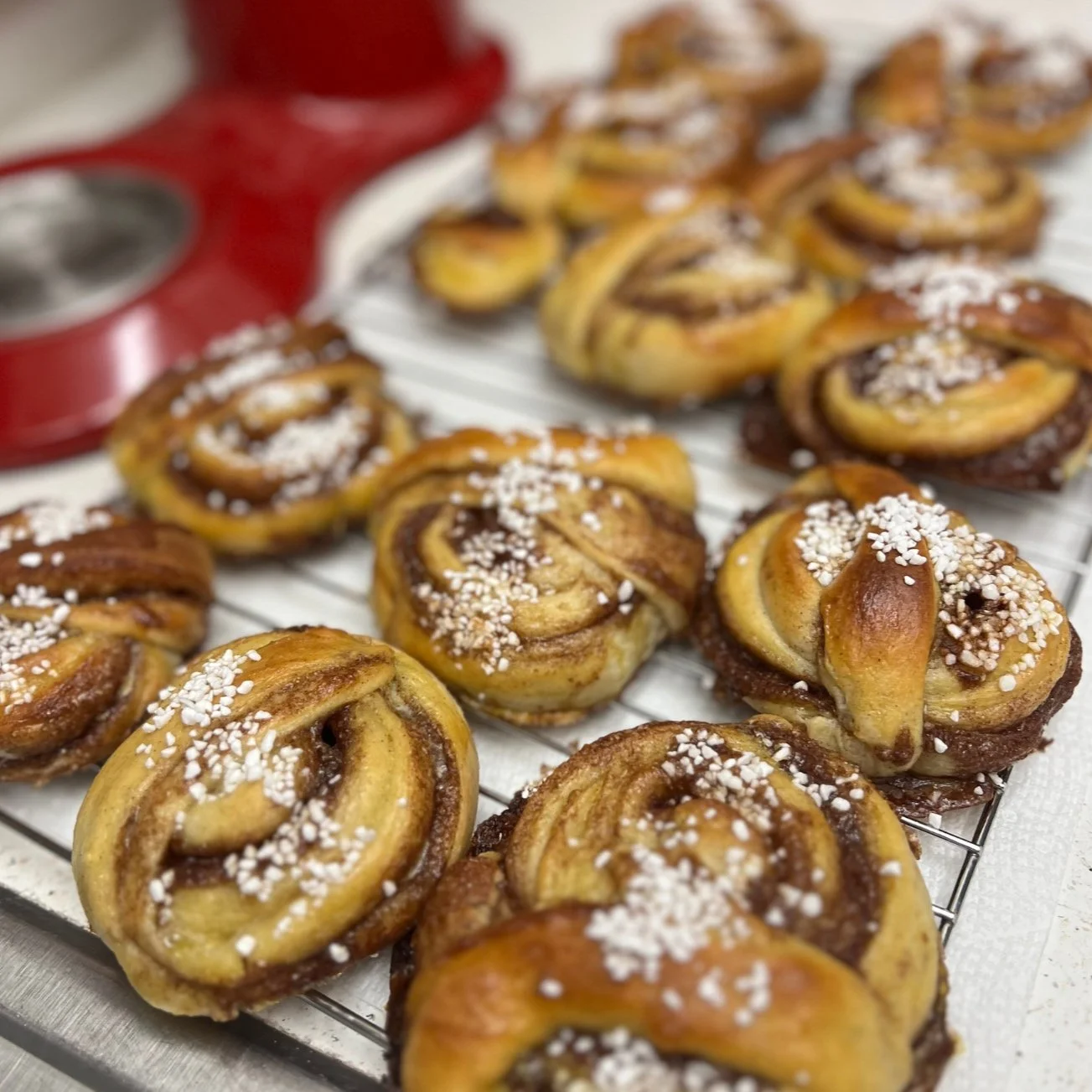 Freshly baked cinnamon rolls topped with pearl sugar on a wire cooling rack.