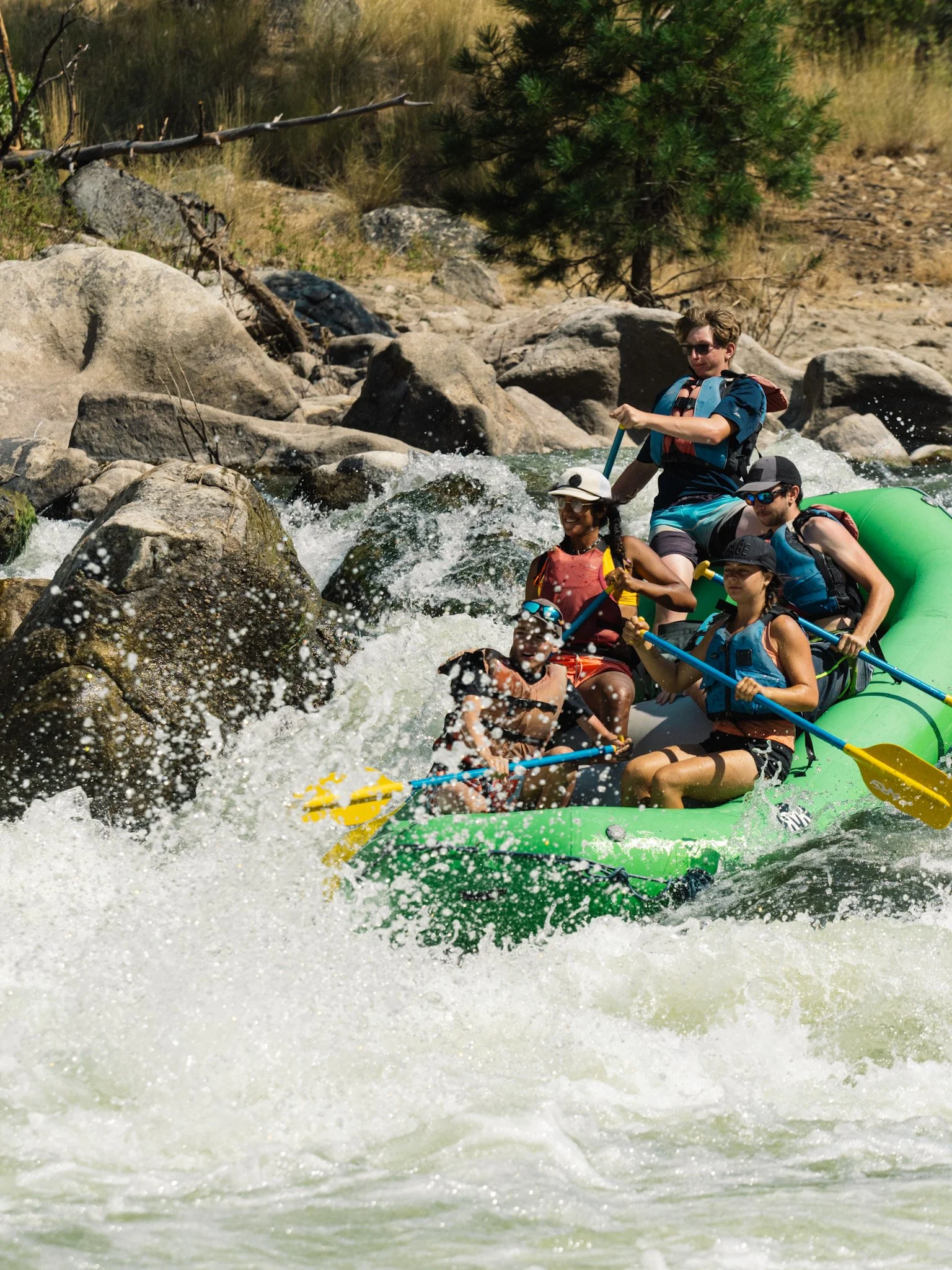 A green raft with passengers maneuver over a steep drop in a rapid. 