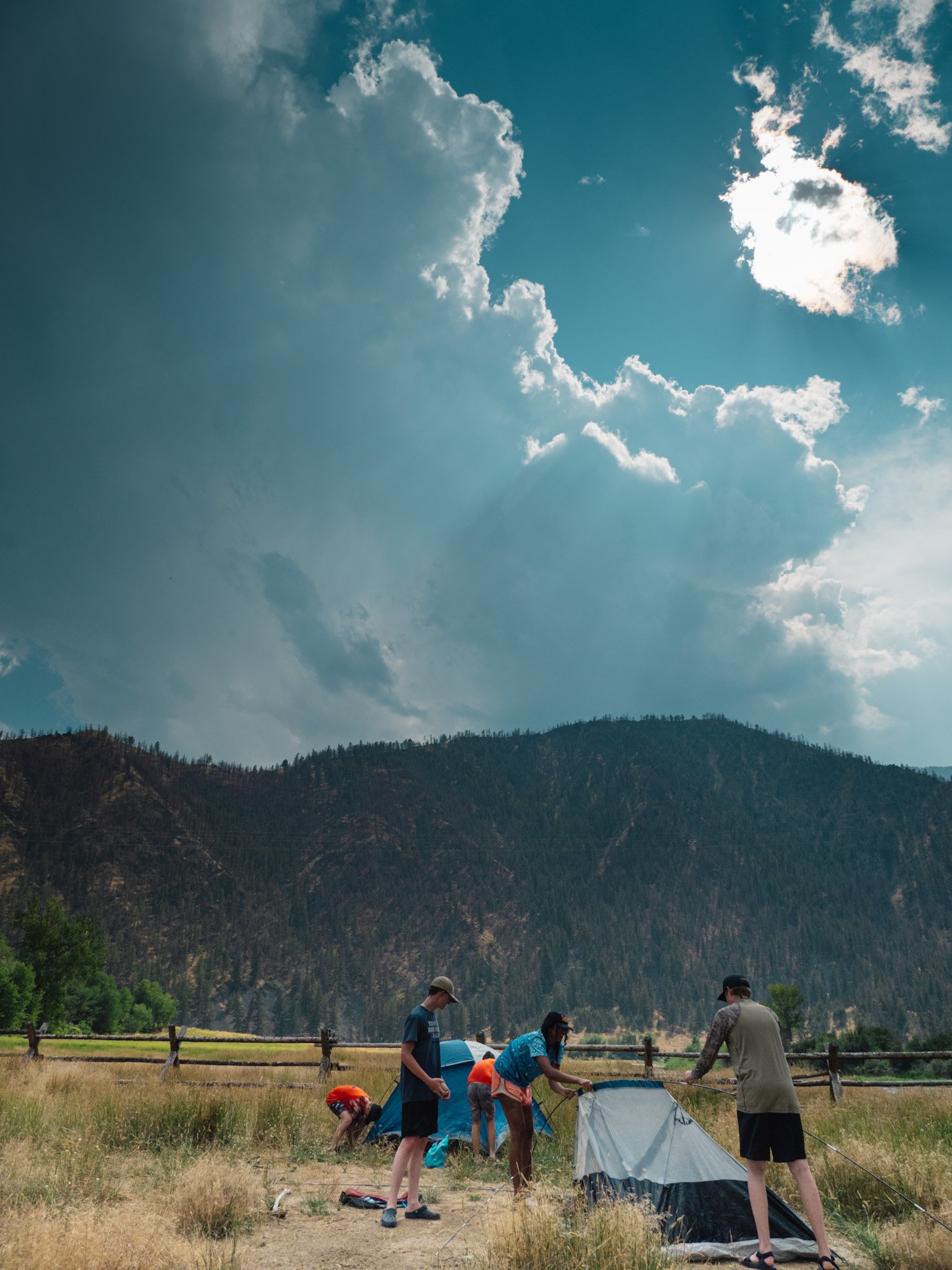 Campers pitch tents with clouds building in the background.