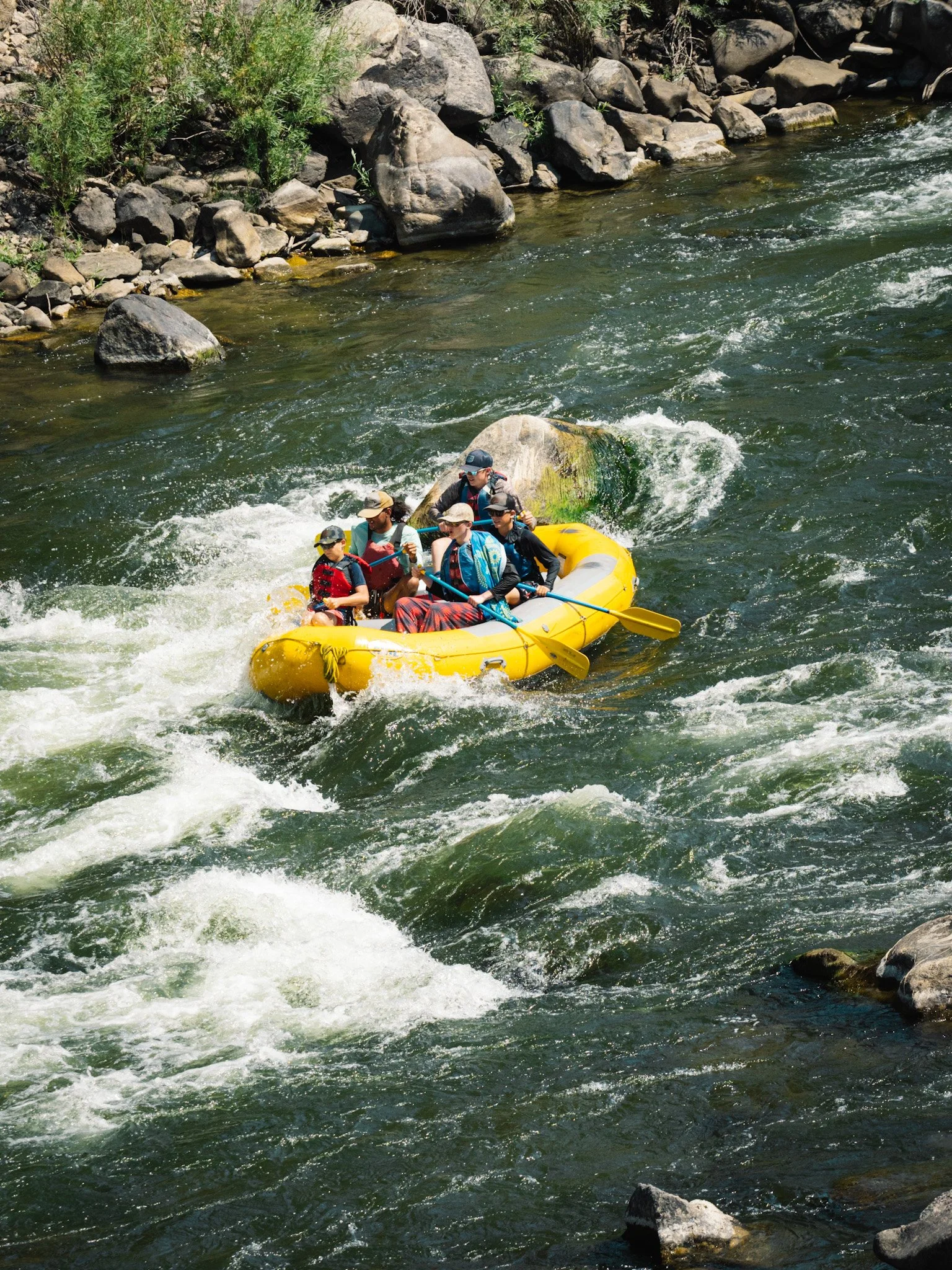 People in a yellow raft paddle through whitewater.