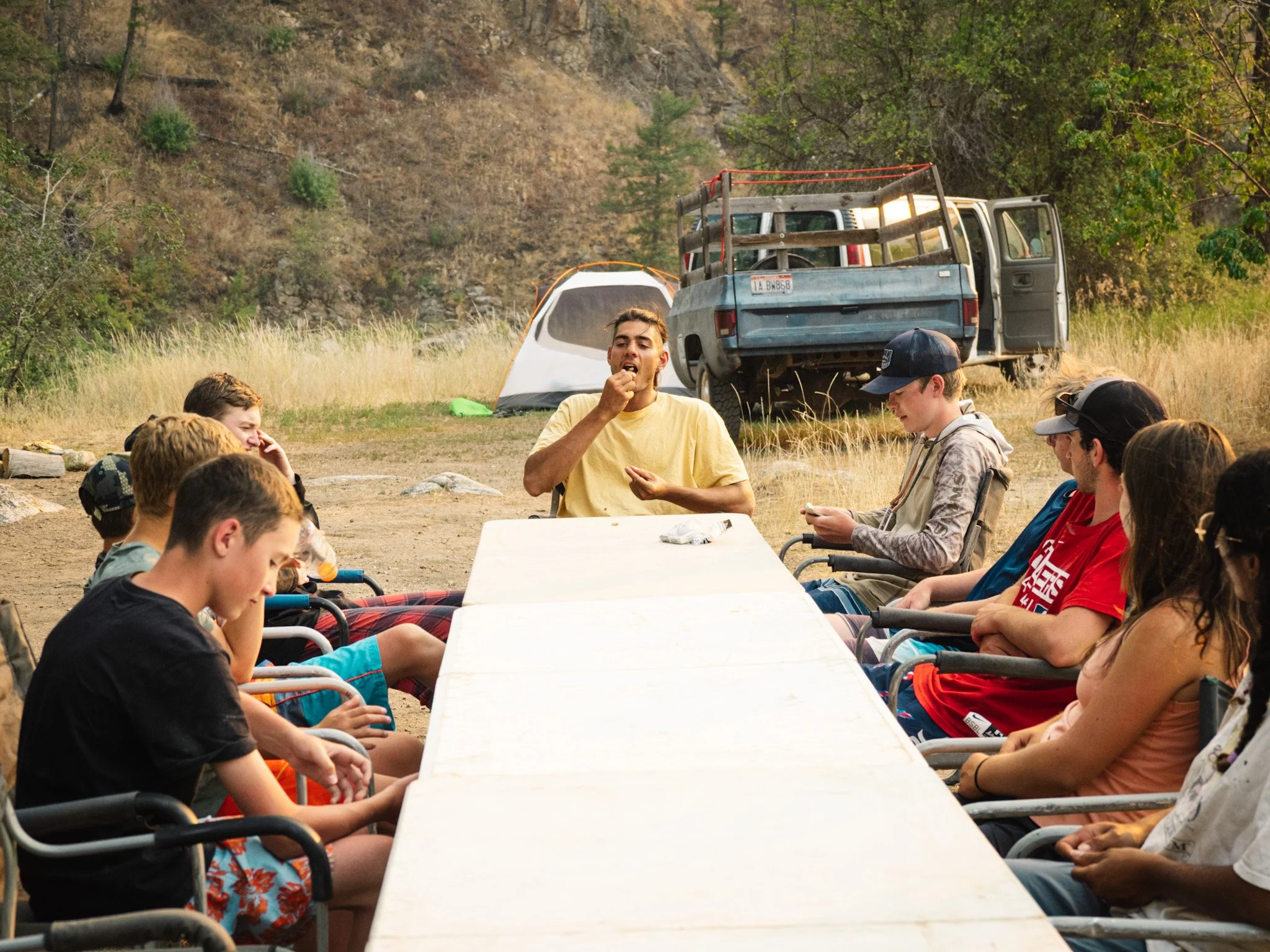 Campers line both sides of a long table engaged in conversation.
