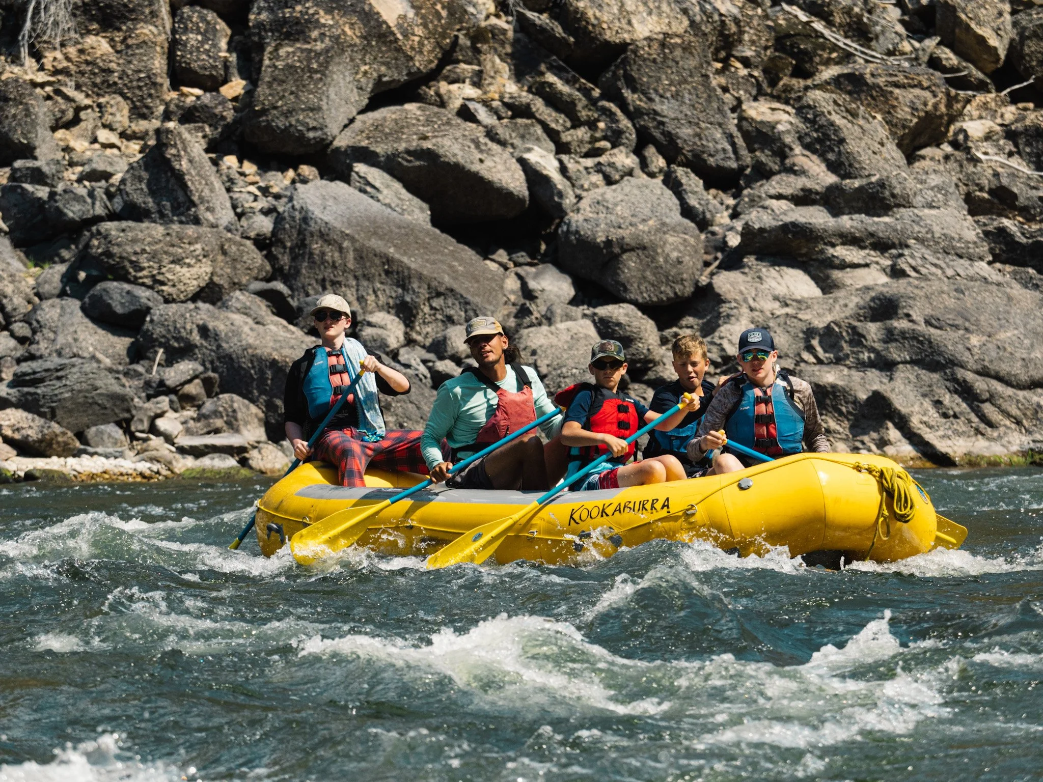 A team of paddlers maneuvers a yellow raft in mild whitewater.