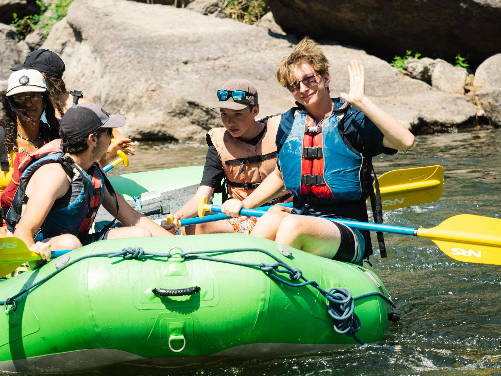 A passenger in the front of green raft waves with one hand.