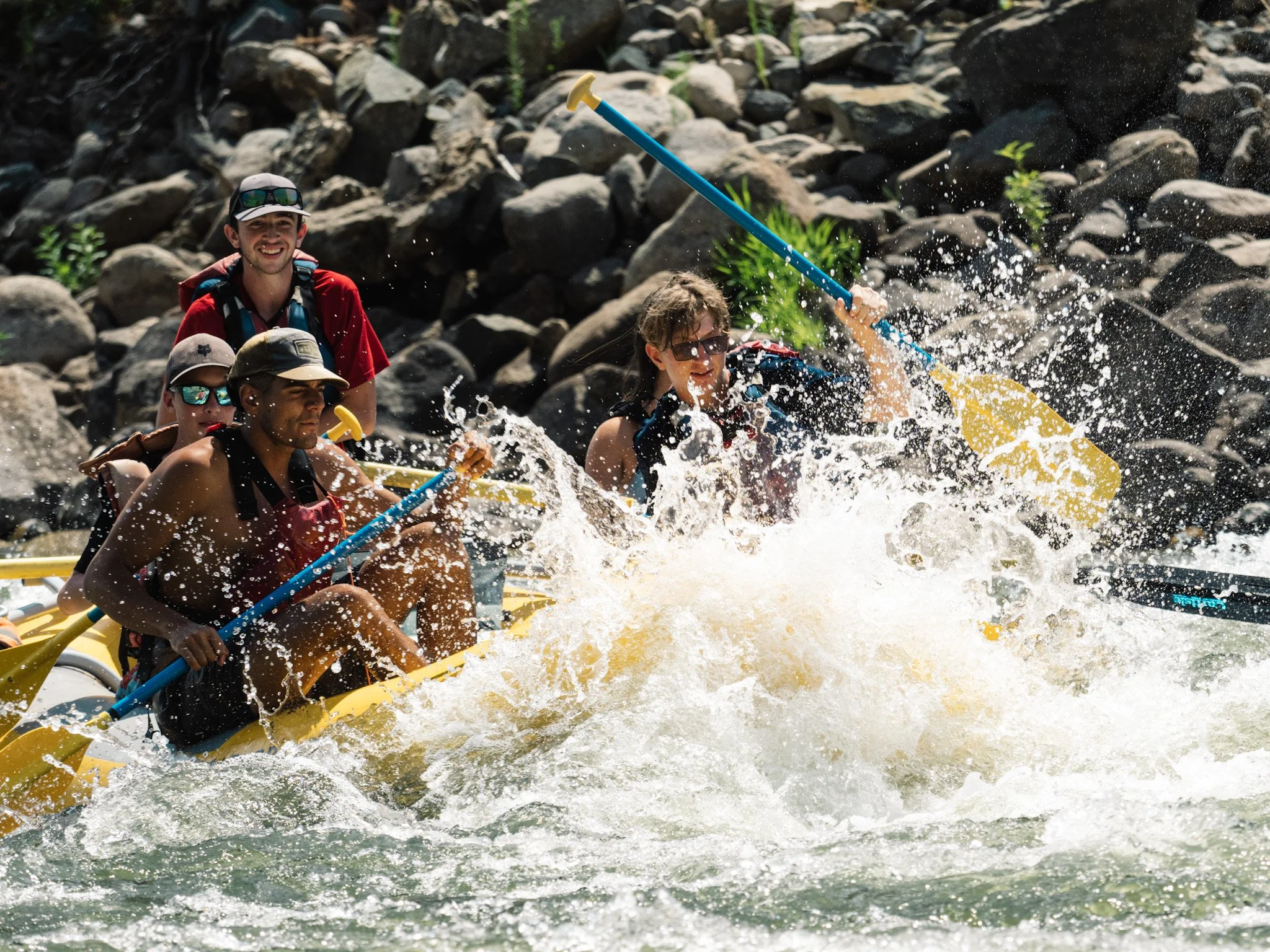 Water splashes high over the bow of a raft while its passengers navigate through whitewater.