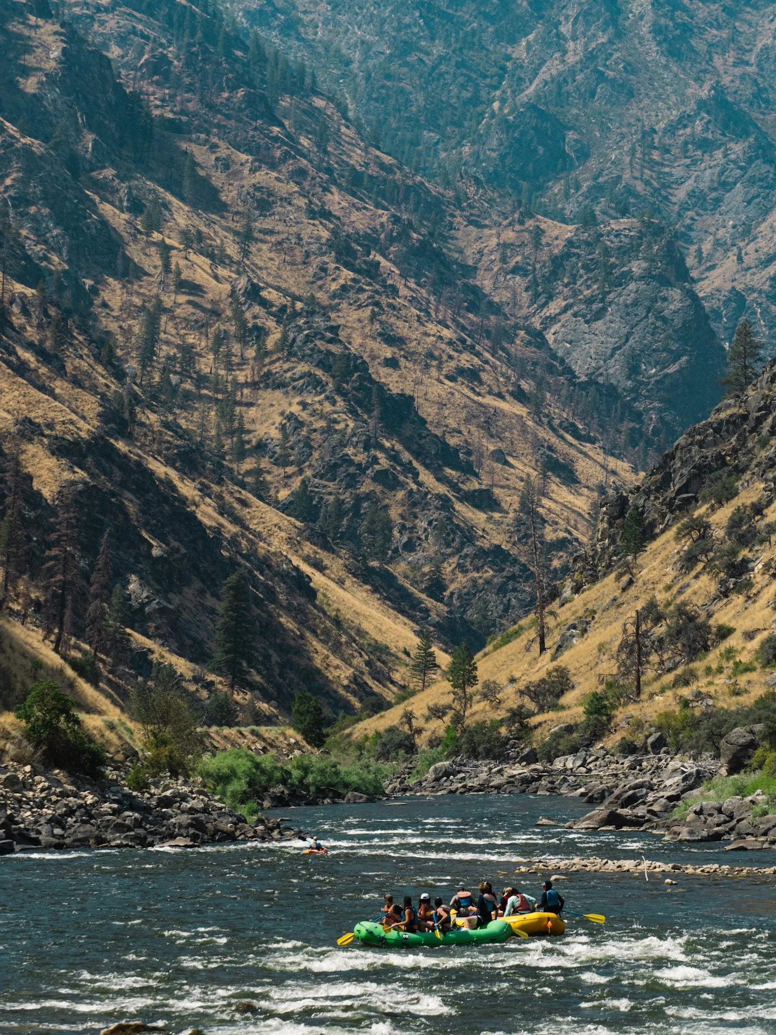 Multiple rafts approach a remote canyon with steep, rocky sides in an arid landscape.