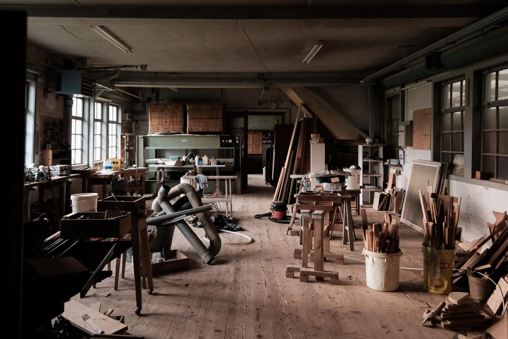 Ein chaotischer Werkraum mit Holzbohlen, Werkzeugen und Maschinen.