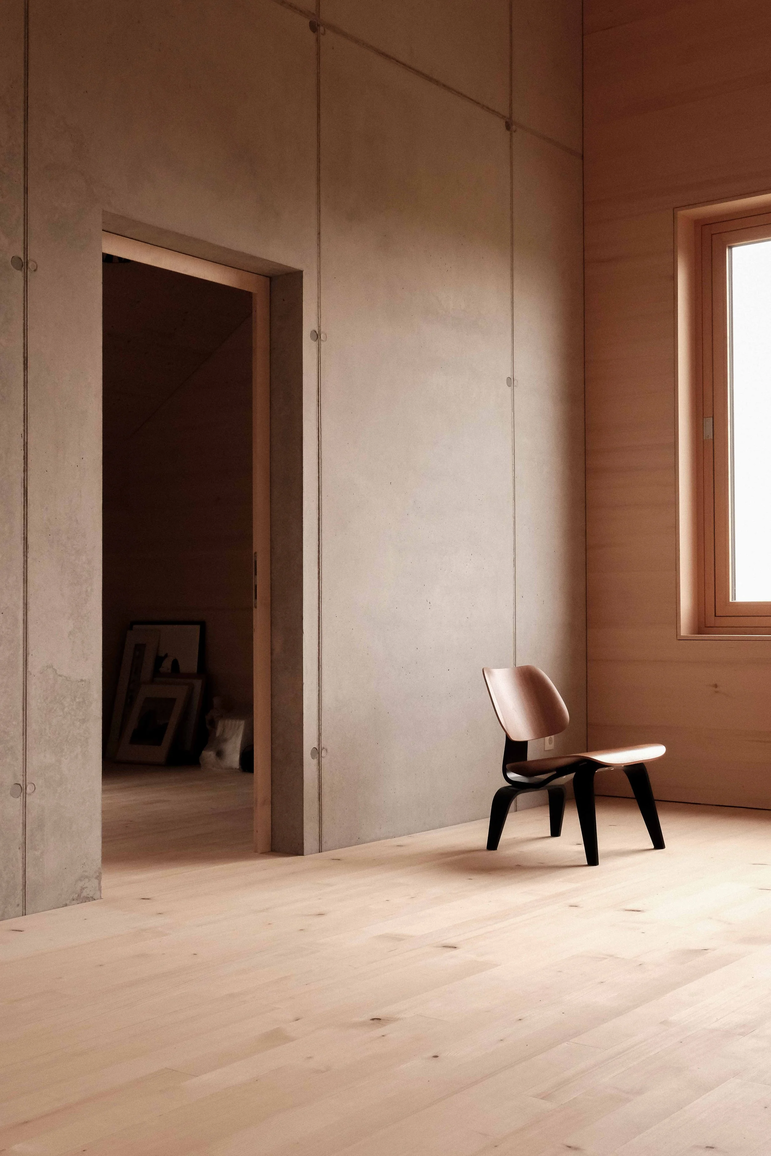 Ein moderner, minimalistischer Raum mit Holzfußboden, einer einzelnen Stuhl und einem Fenster, das Tageslicht hereinlässt.