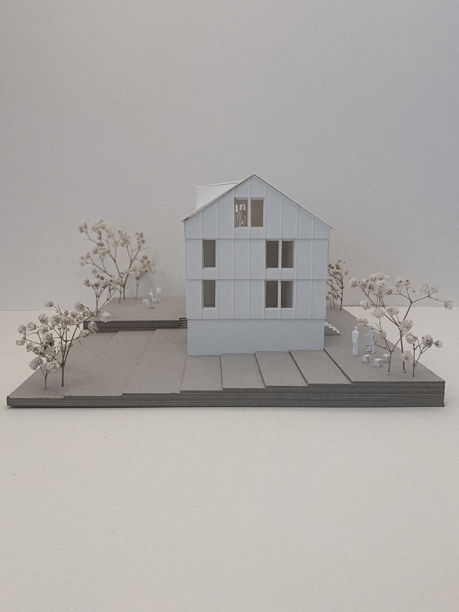 Architekturdia mit einem modernen mehrstöckigen Haus auf einem Modellgrundstück, umgeben von Bäumen und Miniaturfiguren.