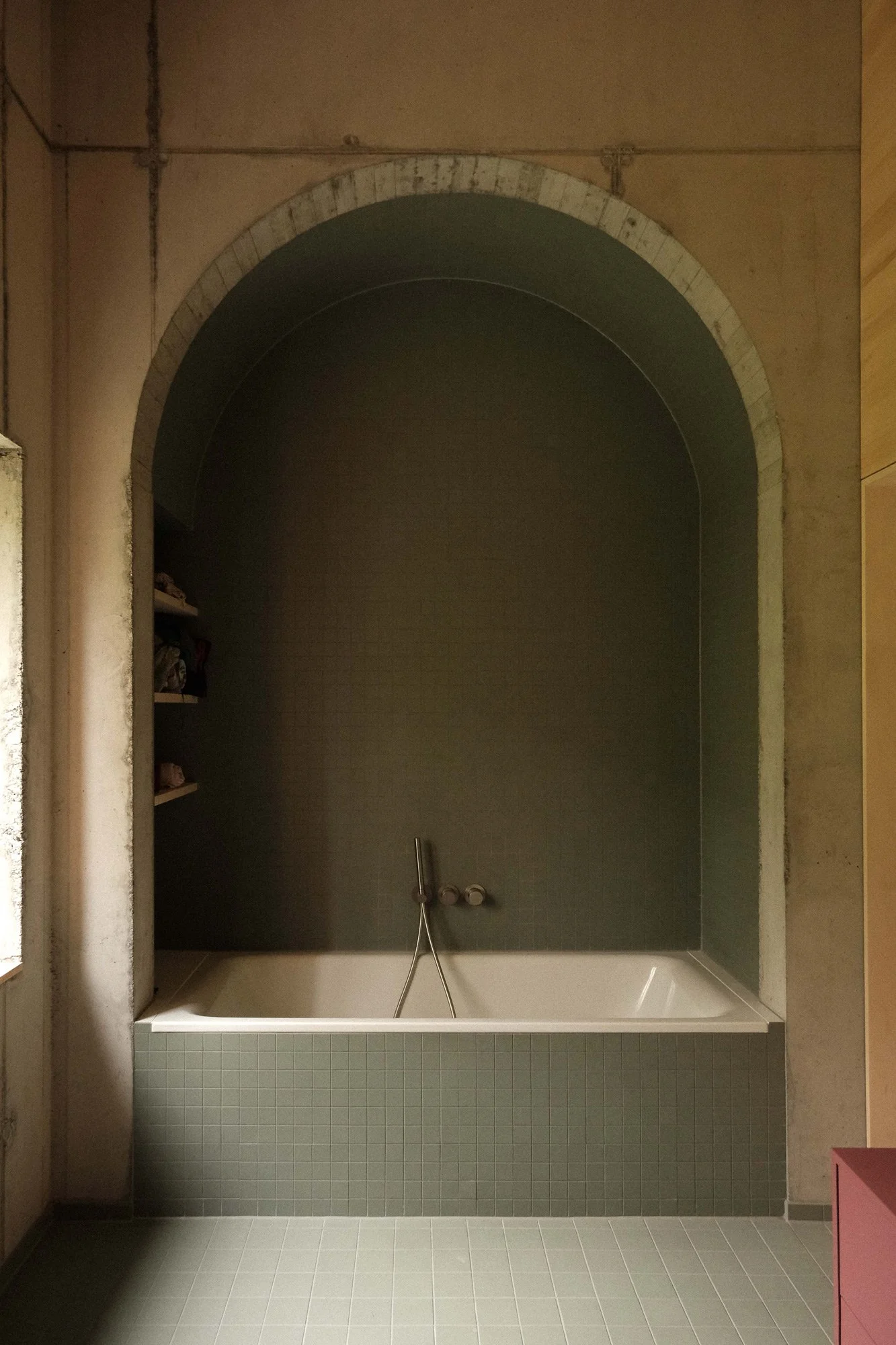 Ein Bad mit Badewanne, grünen Fliesen, Wandnischen und einer Dusche