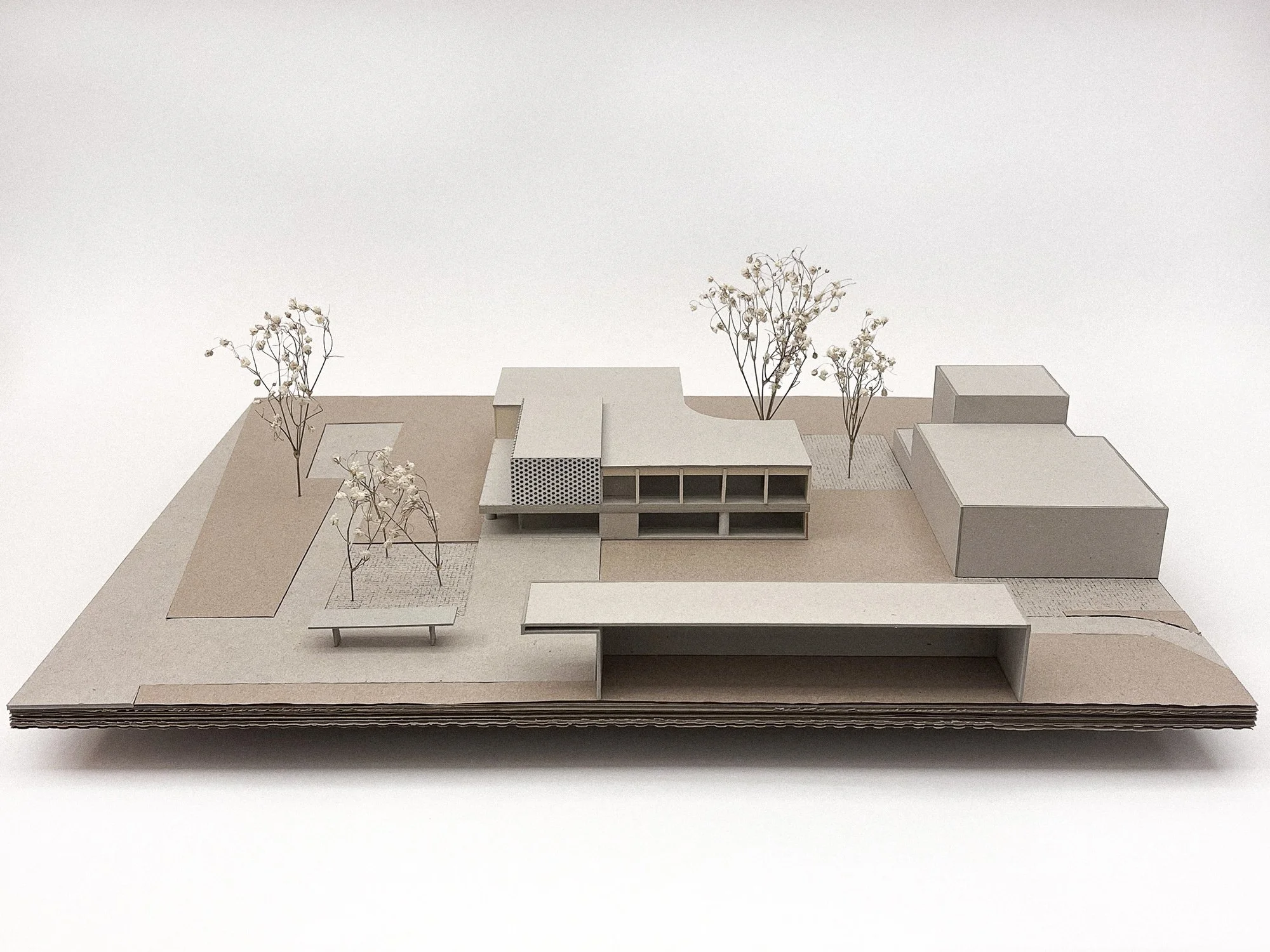 Architekturmodell eines modernen Gebäudes mit Bäumen und Wegen auf einem weißen Hintergrund.