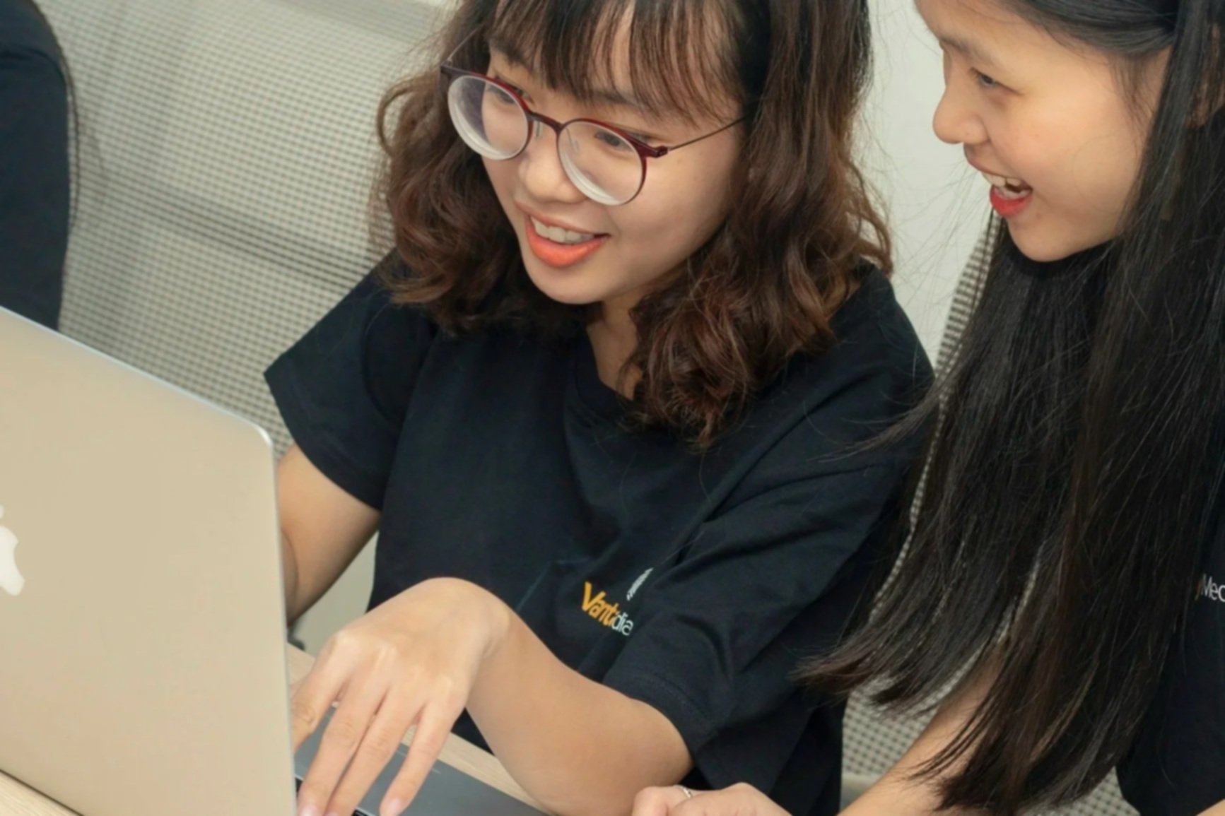 Two students smiling and collaborating while looking at a laptop together during a classroom session.