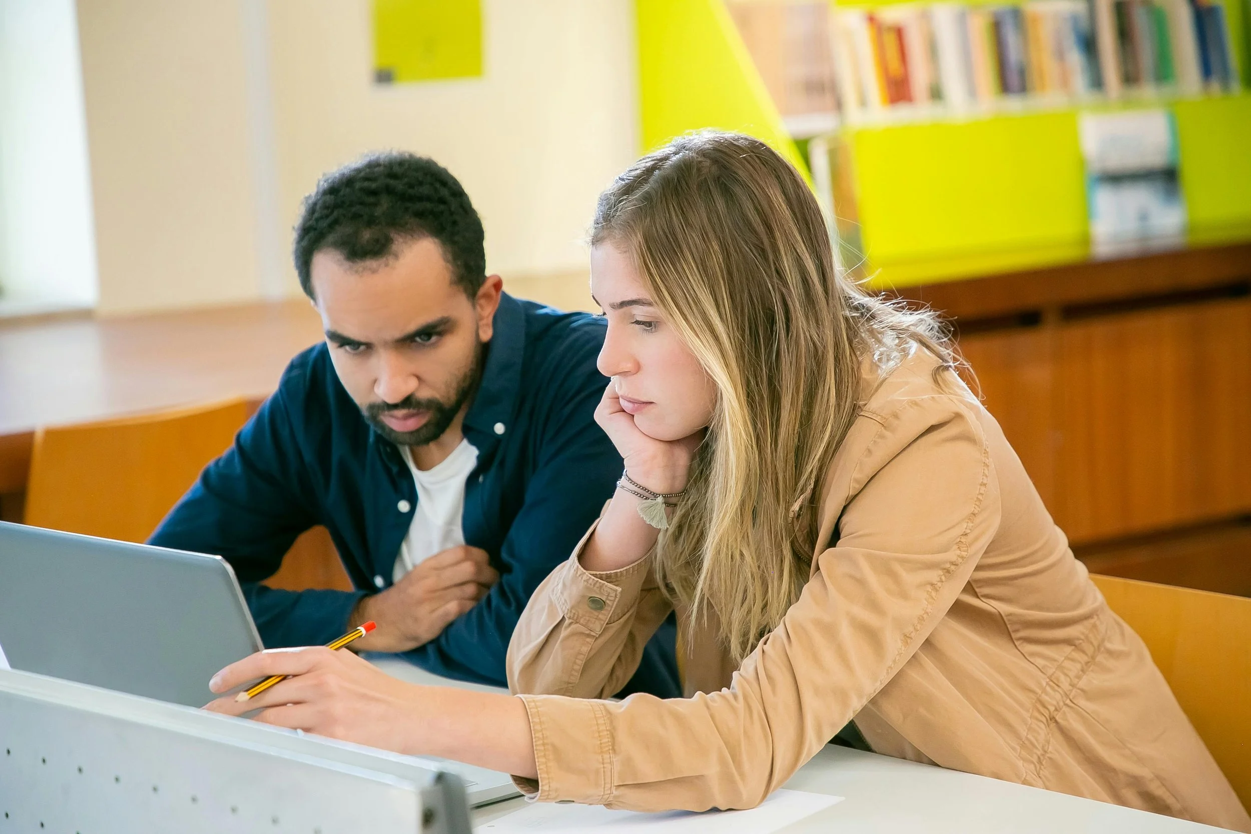 Two teachers use a laptop in a school library to collaborate on curriculum planning.