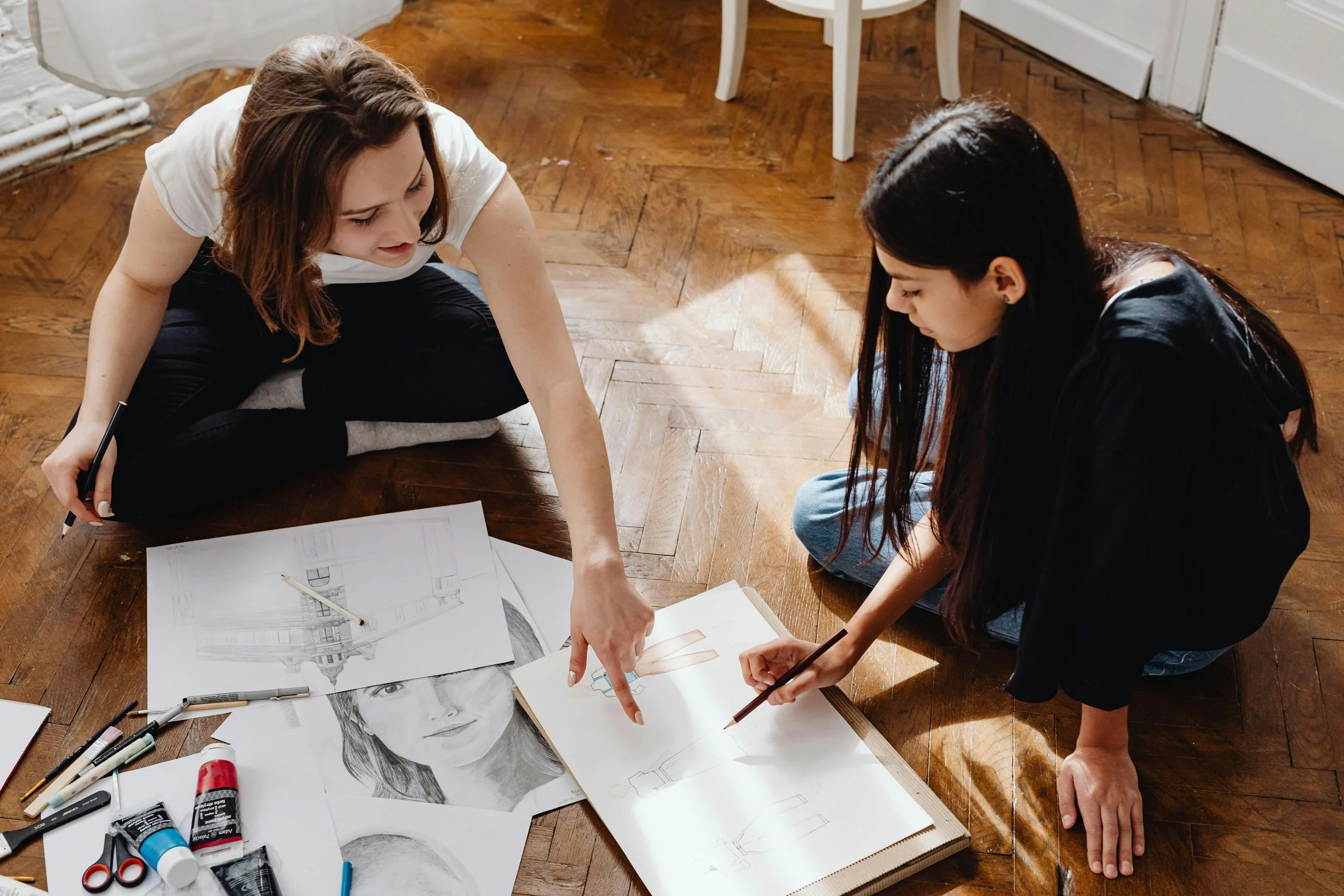 Two students collaborating on an interdisciplinary art and design project while reviewing sketches and creative work on the floor.