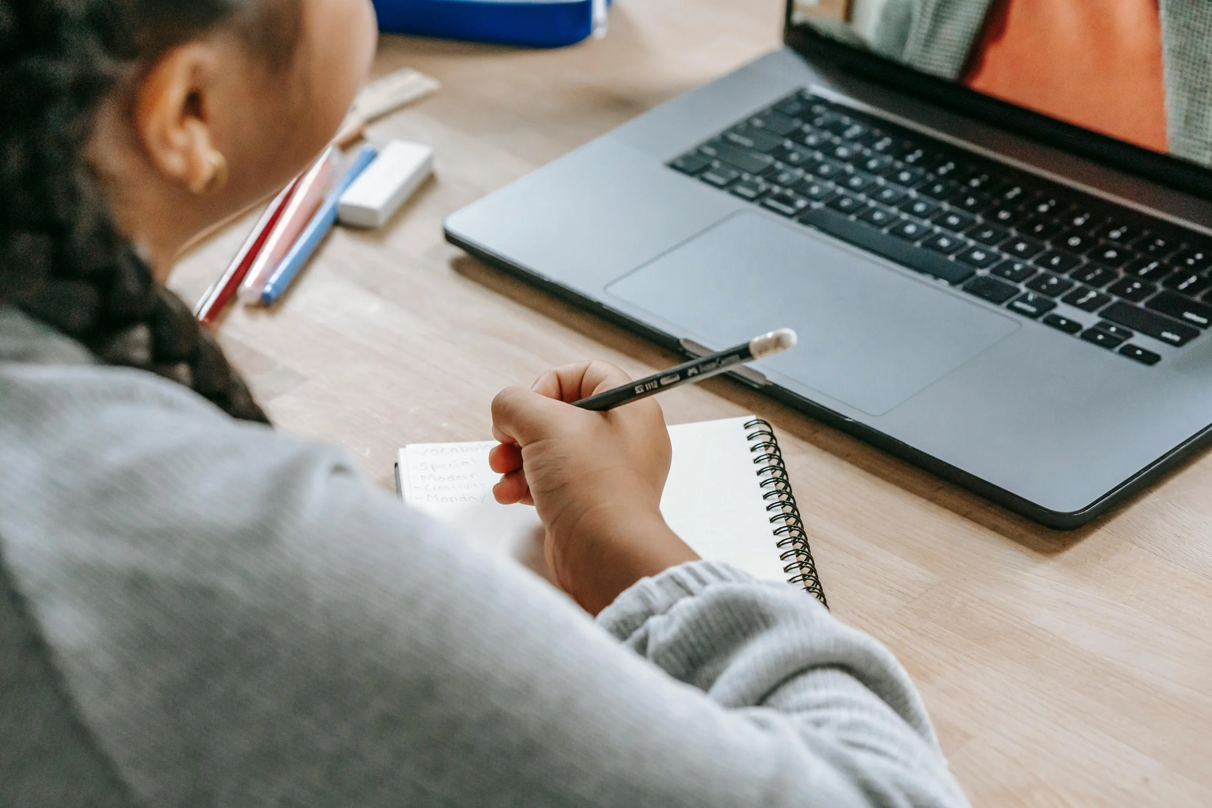 Student writing notes while viewing feedback or instruction on a laptop during an online learning session.