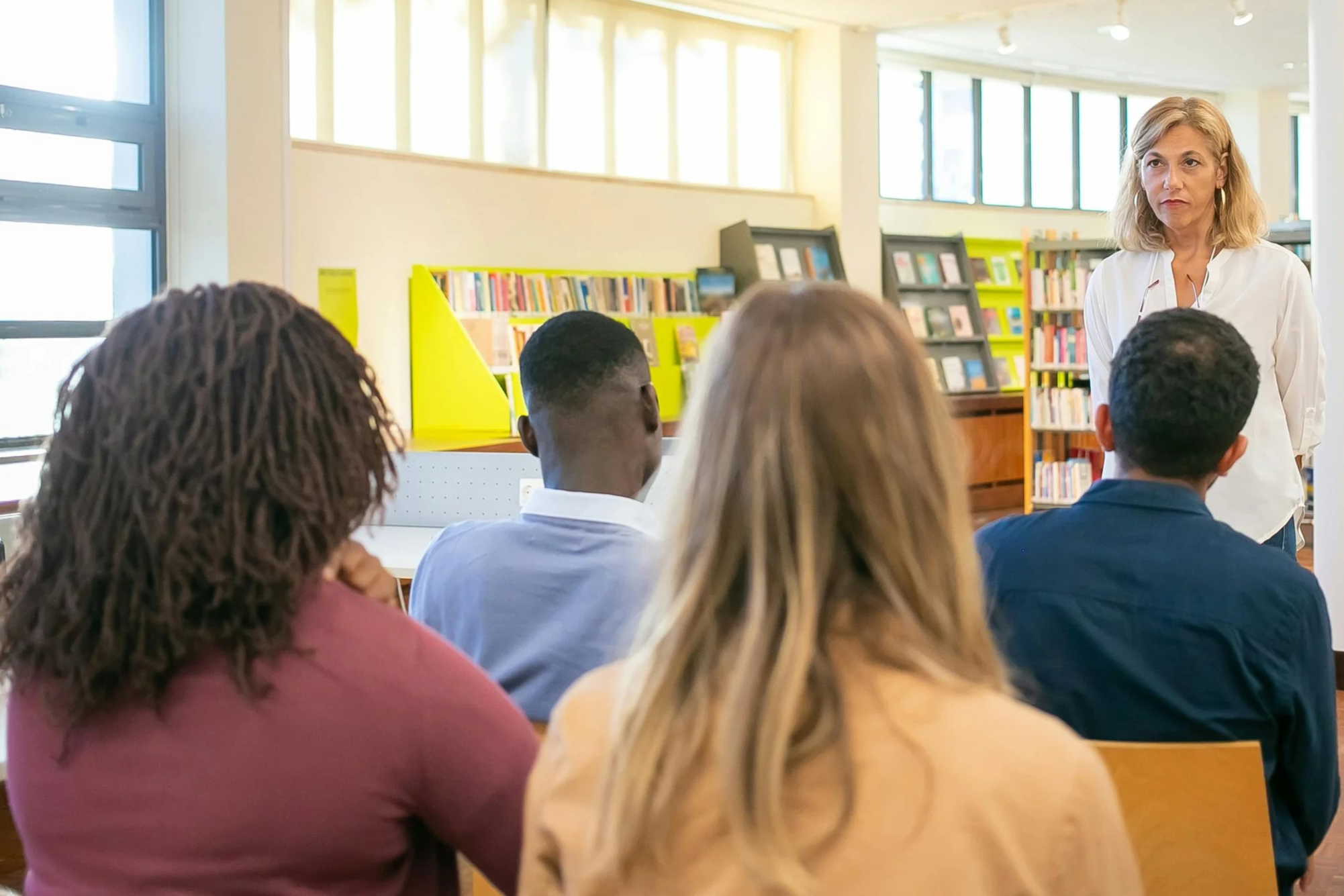 A school administrator leads a professional development session for four seated teachers, listening.