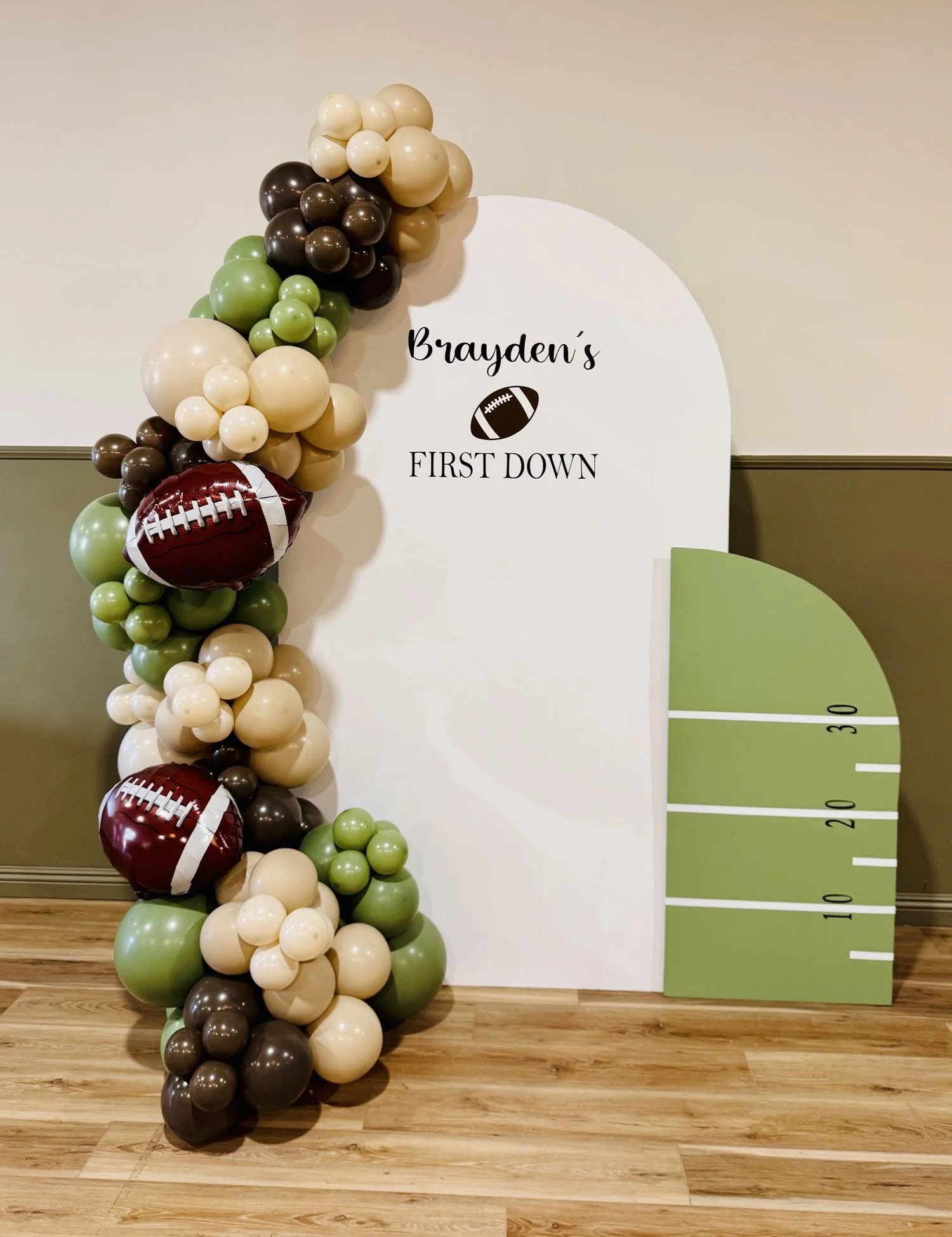 Decorative display for a first birthday party with balloons in football-team colors, a football-shaped balloon, and a height chart on the wall.