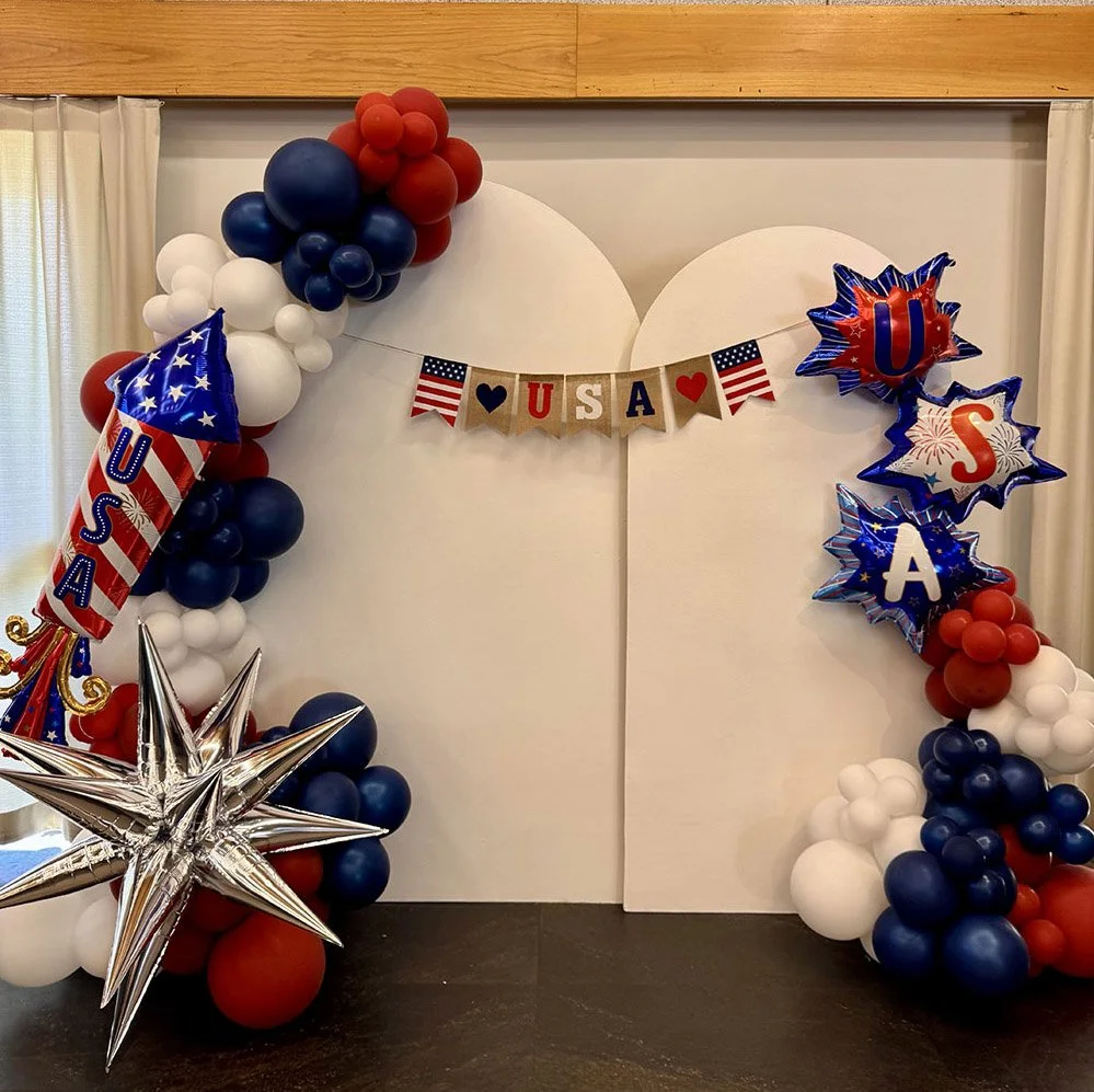 Patriotic American-themed balloon arch with red, white, and blue balloons, star-shaped balloons, and banners spelling out "U S A" and "U S A" with small American flags.