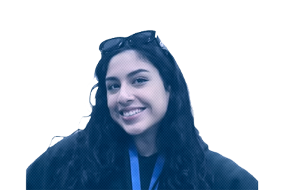 A young woman with long curly hair, smiling, wearing a dark hoodie with blue accents, against a plain background.