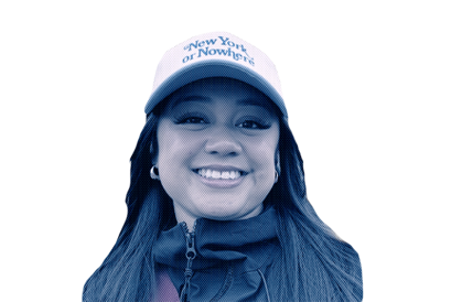 A young woman smiling, wearing a white cap with blue text and a dark jacket.