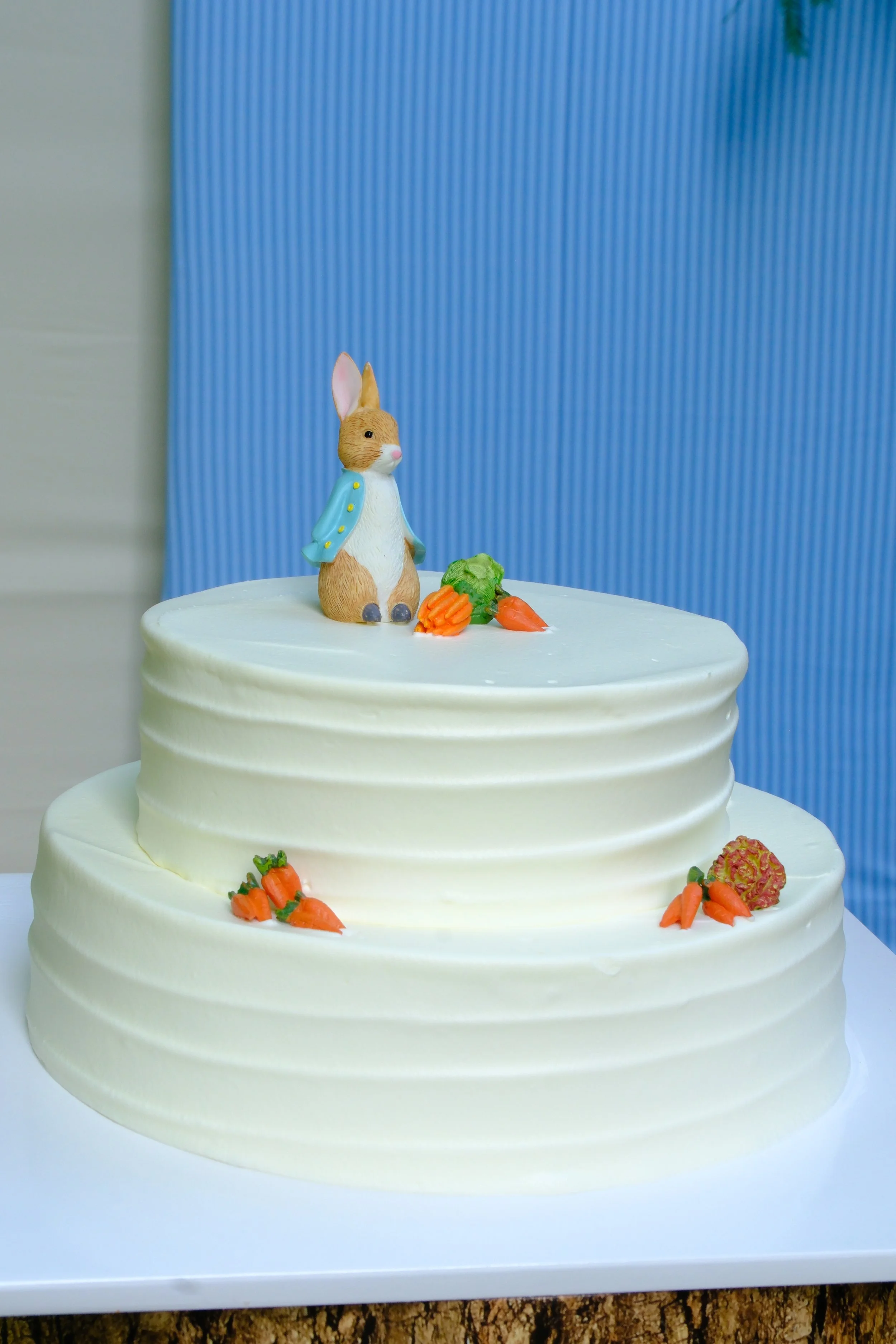 This charming Peter Rabbit-inspired cake is the perfect centerpiece for a whimsical baby shower or spring celebration. Featuring smooth white buttercream, delicate carrot decorations, and an adorable Peter Rabbit topper, it blends storybook nostalgia