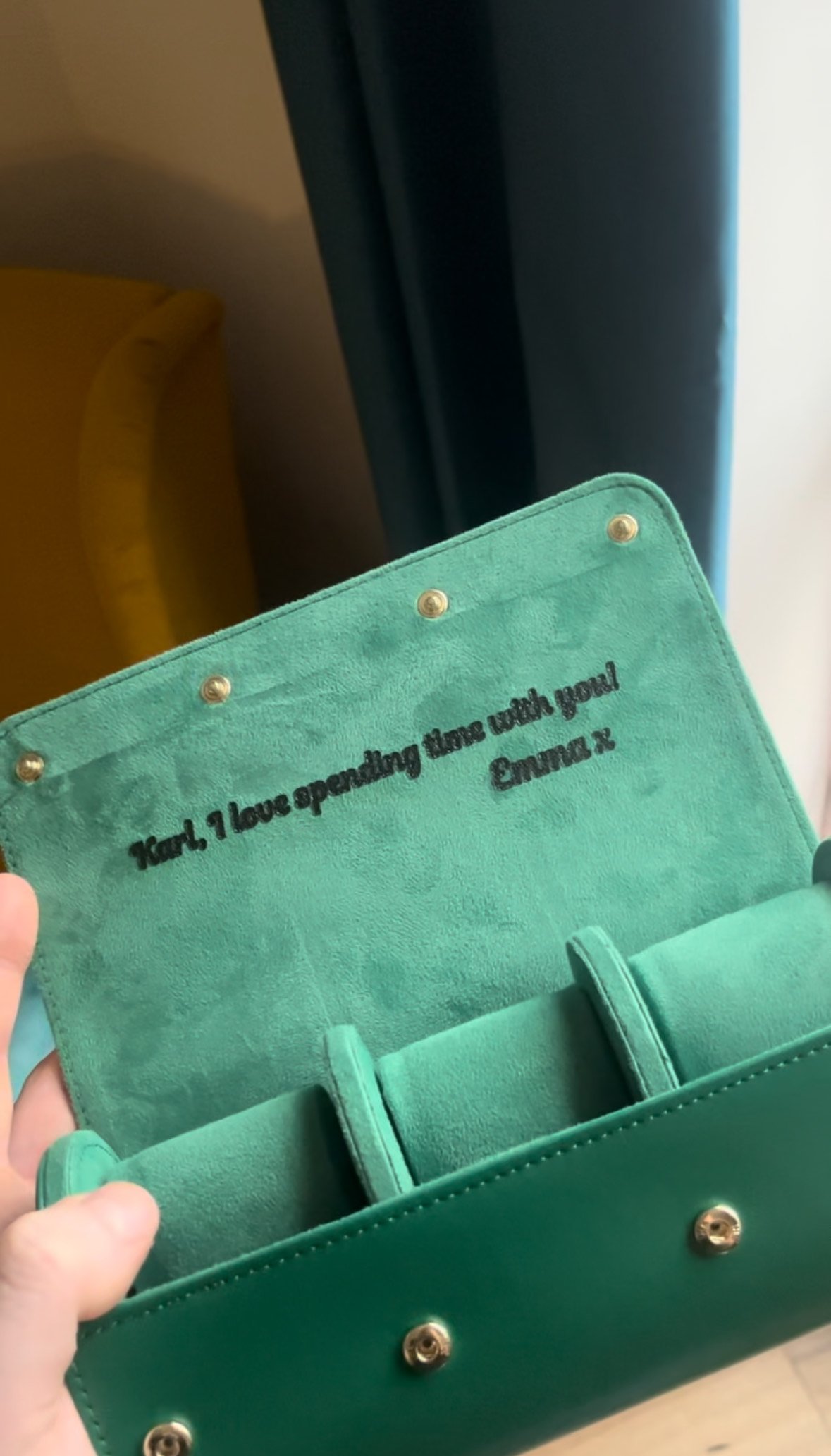 Open green bag with a personalized message inside, reading "Karl, I love spending time with you! Emma x". The bag is held open by a hand, showing gold button details and sections for storage.