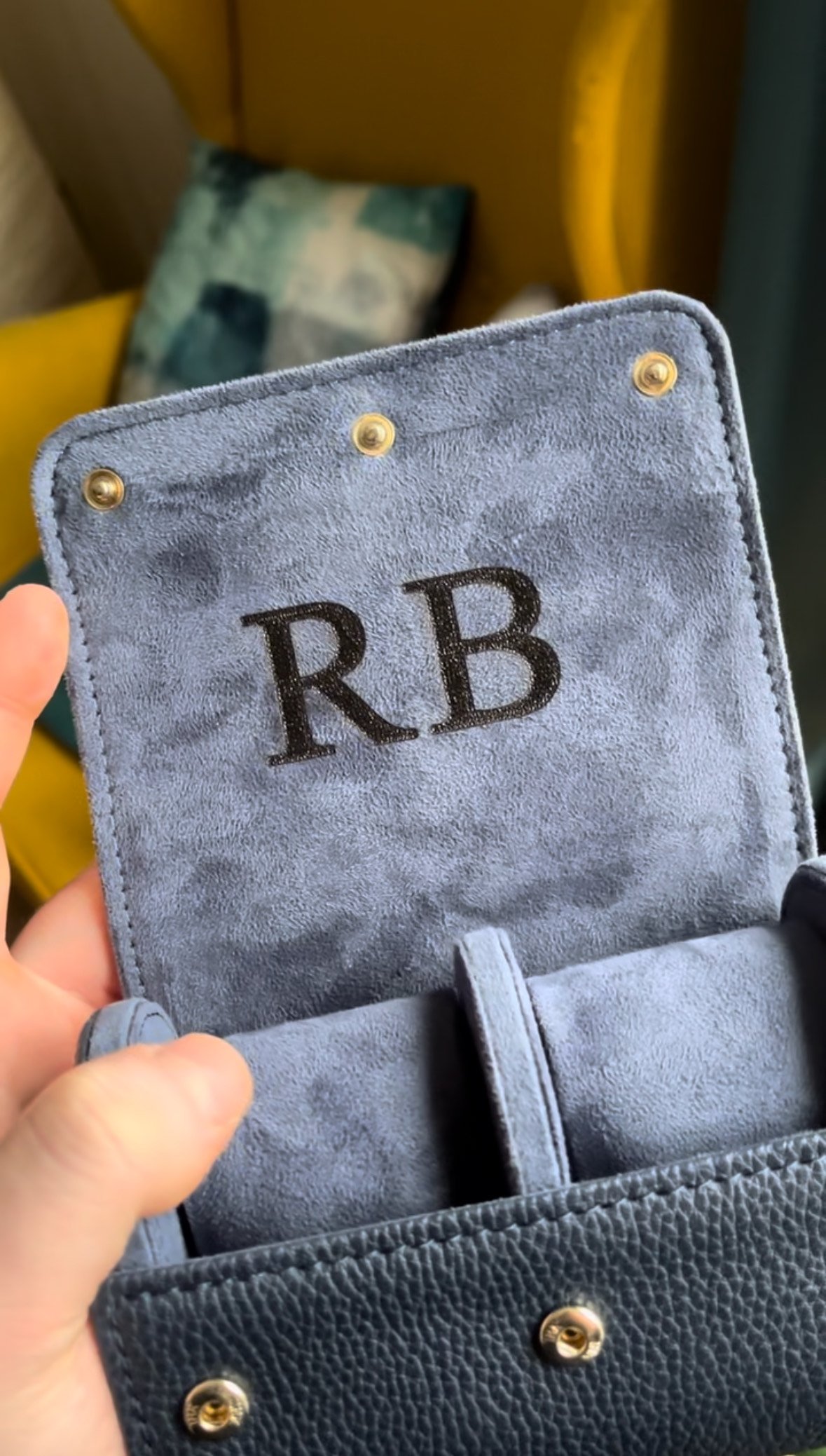 Close-up of a blue suede fabric with initials 'RB' and gold button details.