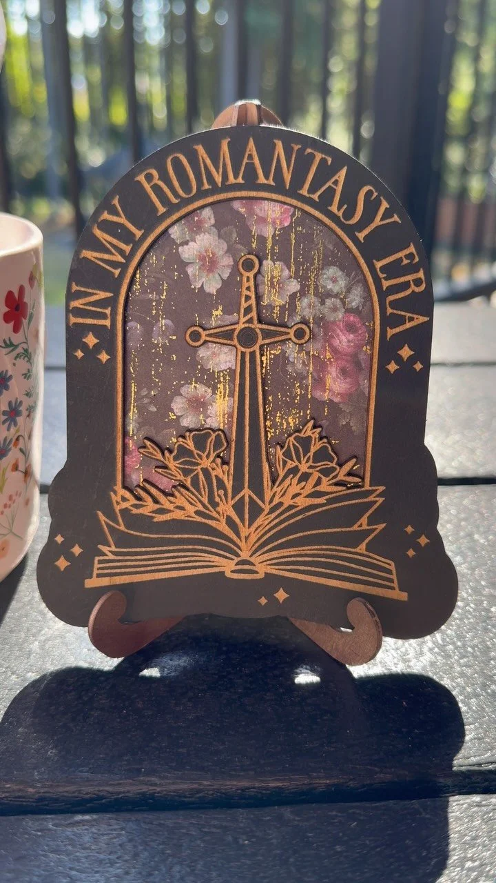 I found the cutest bookish merch at @plottwistpastries 📚 Do you even read #romantasy if you don’t have a gilded wooden sign on your bookshelf? 💖 #bookstagram #booktok #momswhoread #readmorebooks #fantasyromancebooks #inmyera