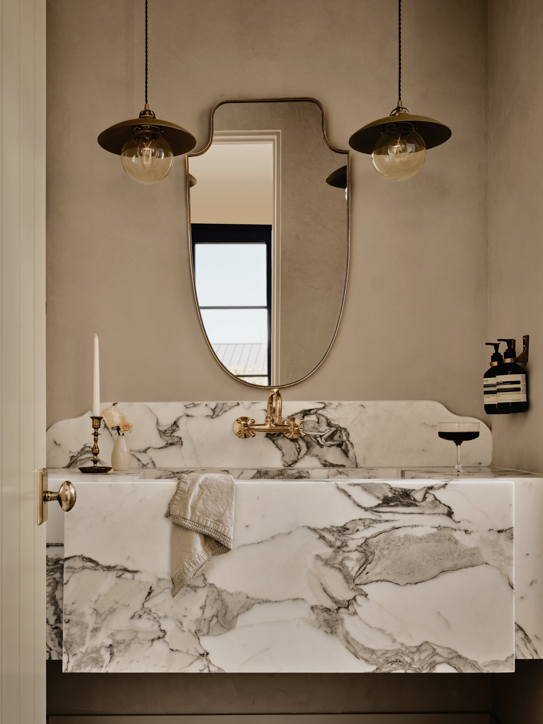 Elegant bathroom with marble vanity, arched mirror, and antique brass sconces by Maeve Design Collective in Paradise Valley, Arizona.