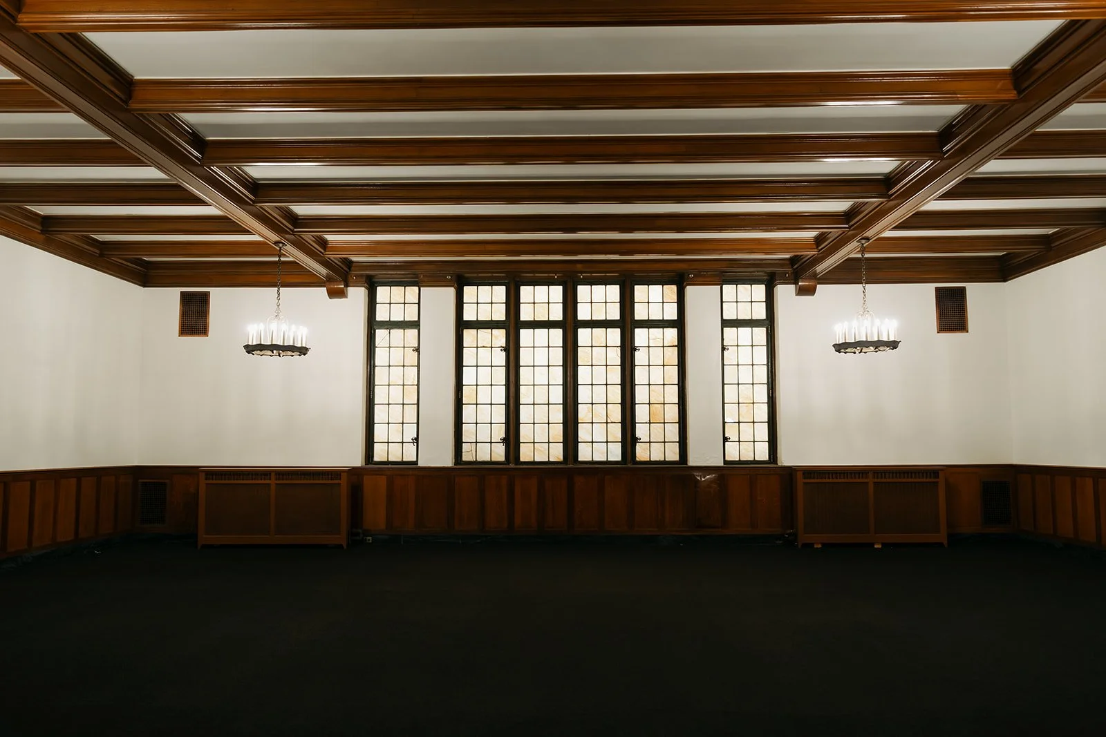 The Osgood Conference room, shown Empty - complete with wood-paneled walls, large stained glass windows, dark carpet, and hanging chandeliers.