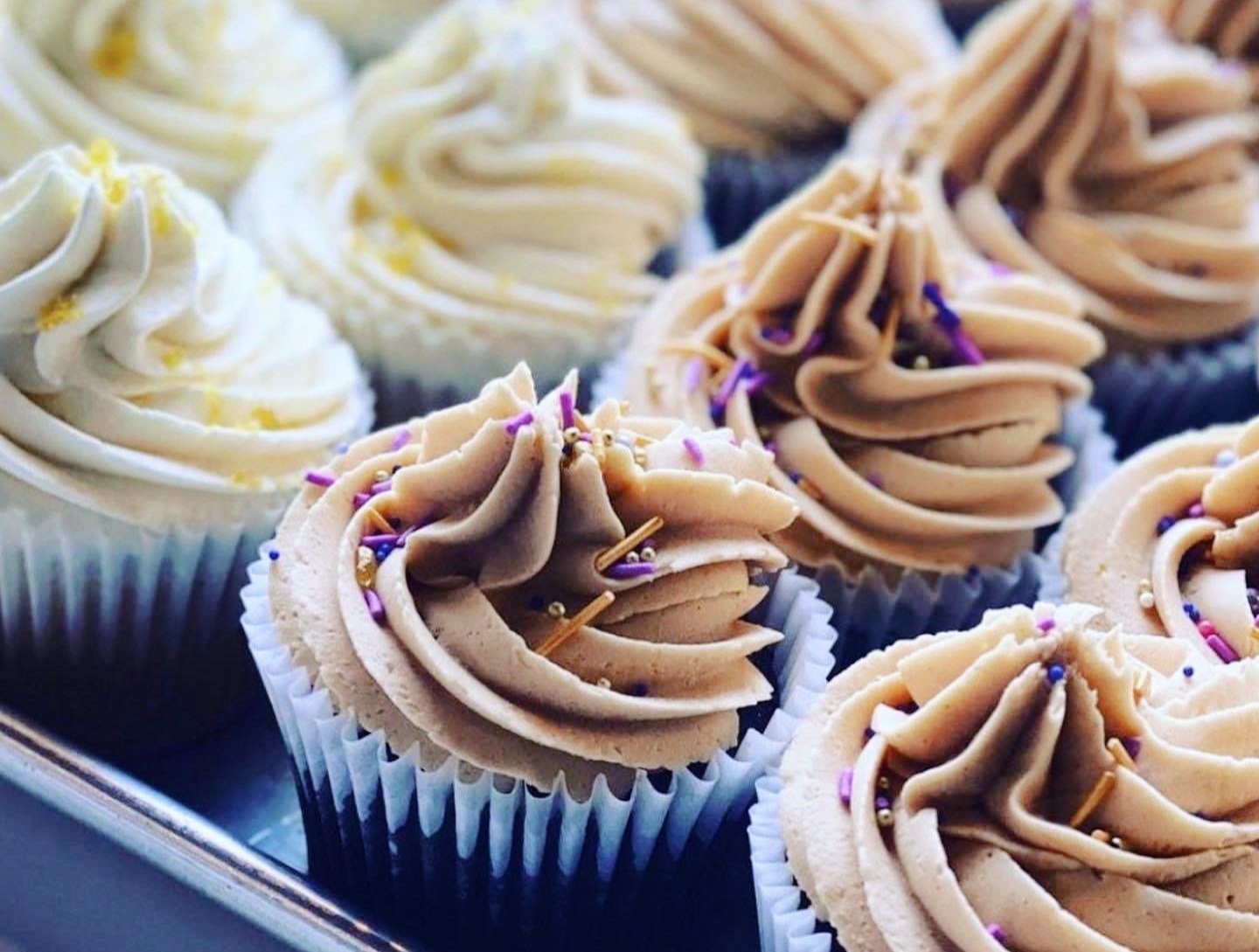 Assorted cupcakes with swirl frosting and sprinkles on a tray.