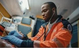 A healthcare worker wearing an orange protective suit and gloves, sitting in an airplane cabin and reading a book.