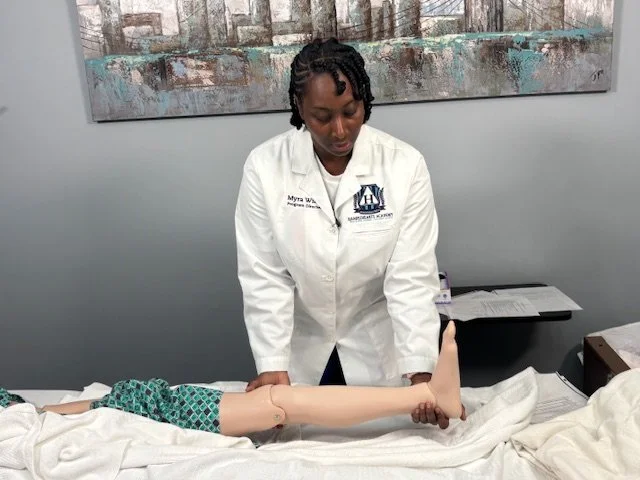 A woman in a white medical coat demonstrating a physical therapy or medical procedure on a mannequin arm in a clinical setting.