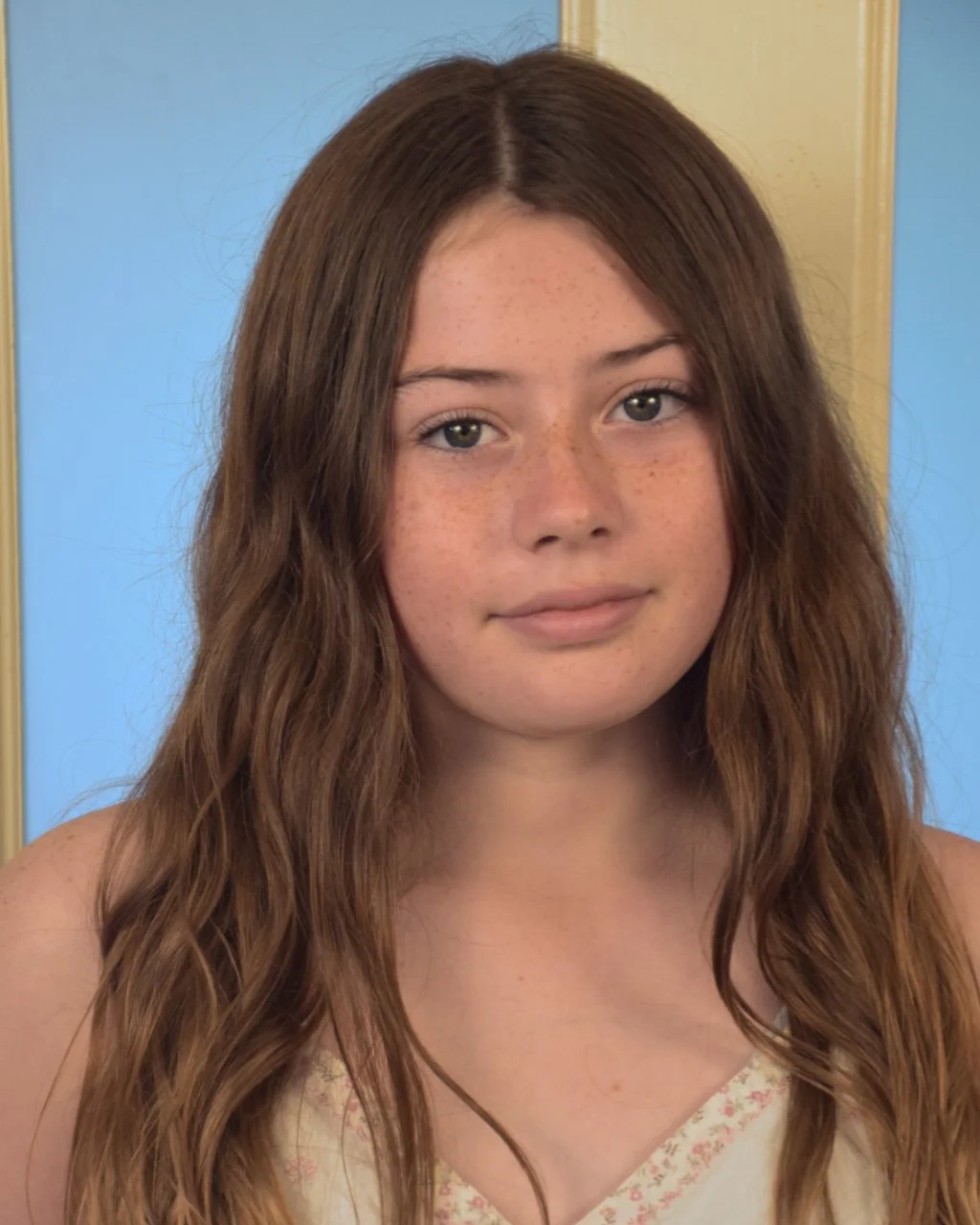 A young woman with long wavy brown hair, blue eyes, and freckles wearing a black shirt and a green stone pendant necklace.