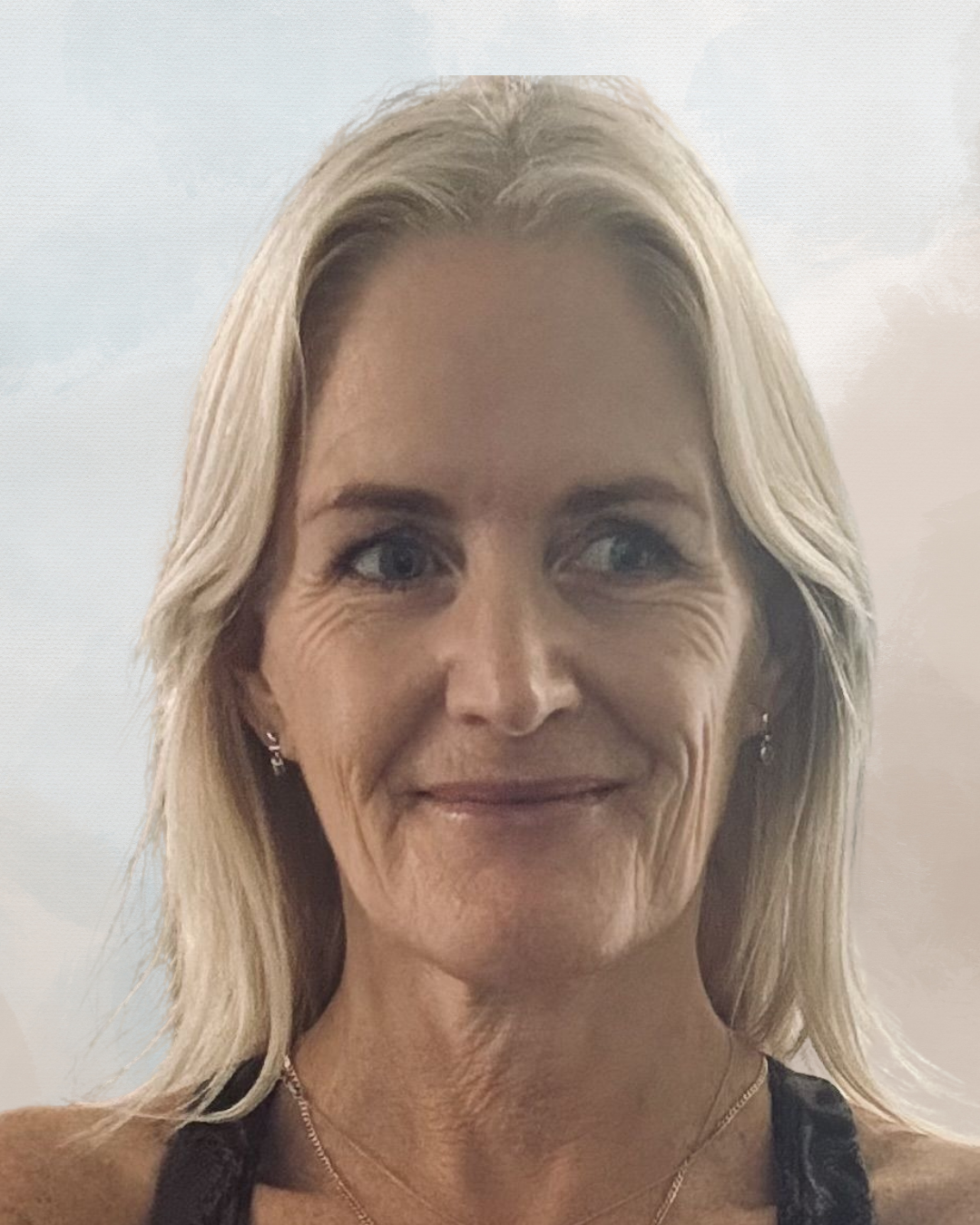 A middle-aged woman with blonde hair smiling in front of a cloudy sky background.