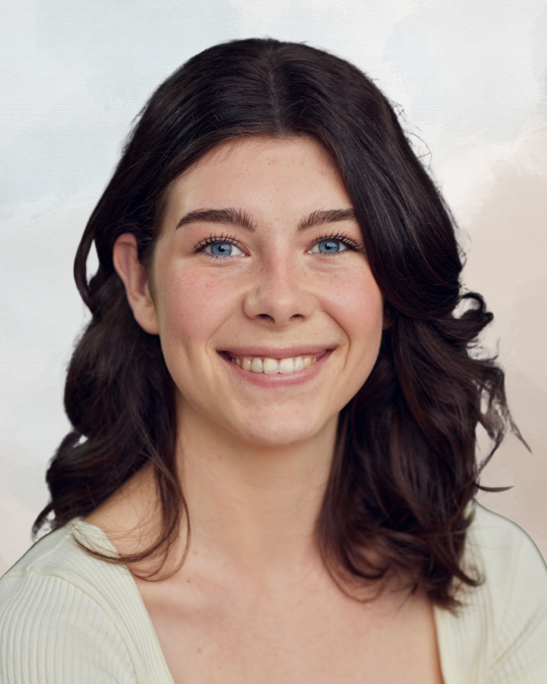 Close-up of a young woman with dark hair, blue eyes, and a smiling expression, wearing a light-colored top.