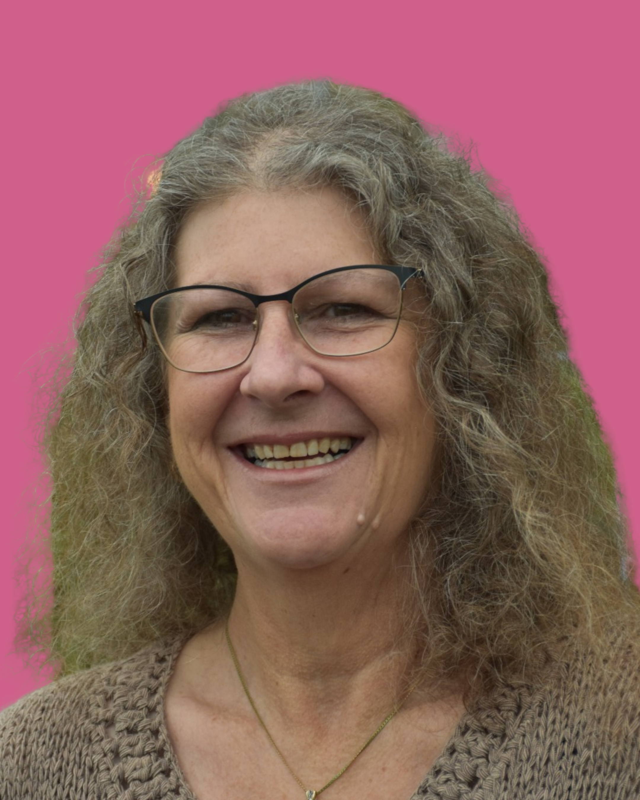 A smiling woman with curly gray hair and glasses, wearing a beige sweater, against a pink background.