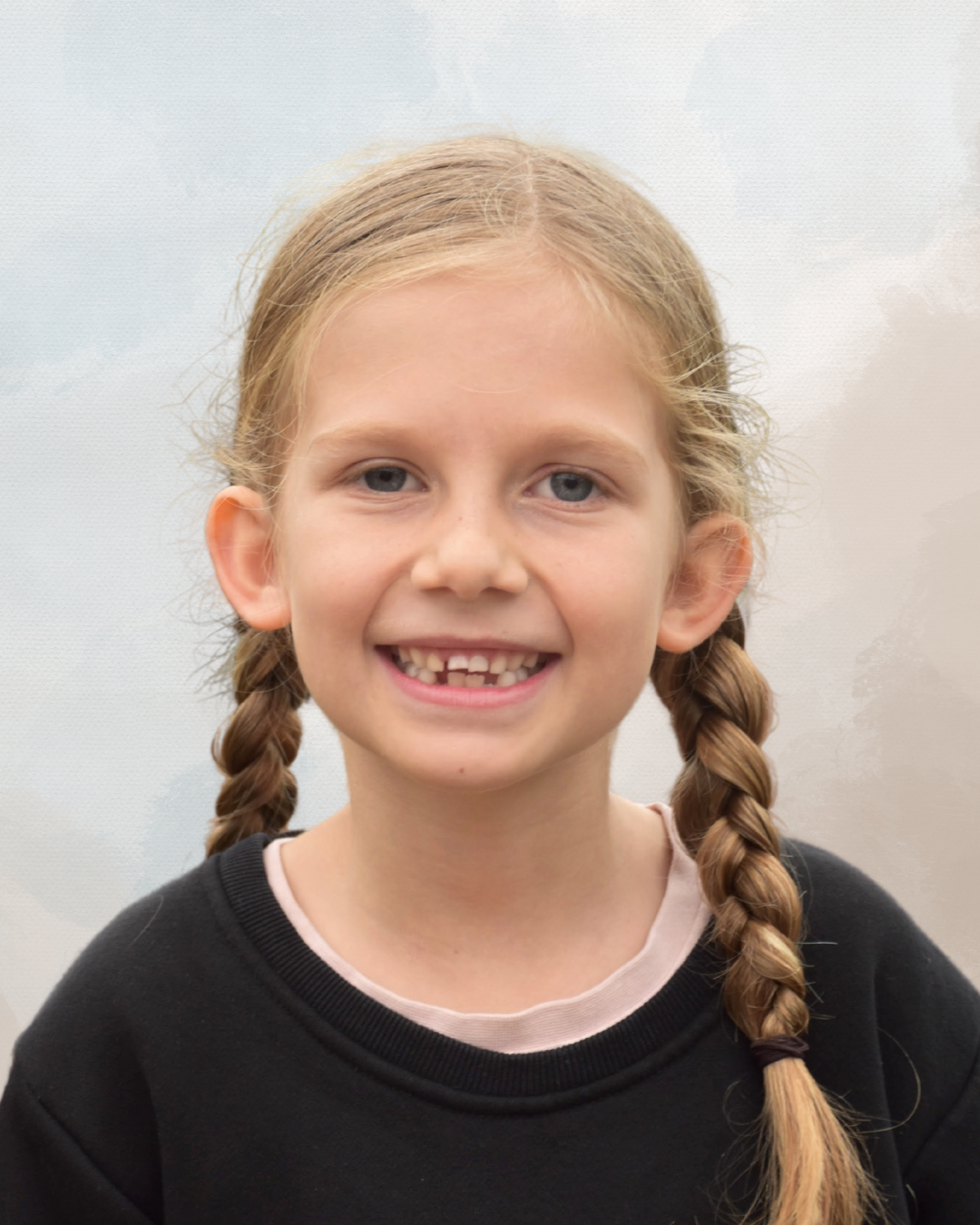 A young girl with blonde hair in braids smiling at the camera, wearing a black sweatshirt.