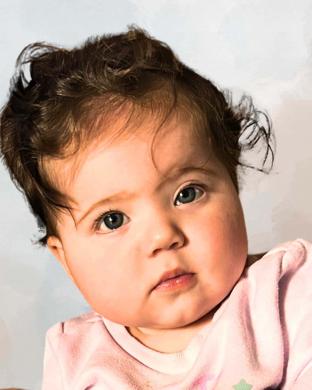Close-up of a young child with curly brown hair and blue eyes, wearing a pink shirt, against a plain background.