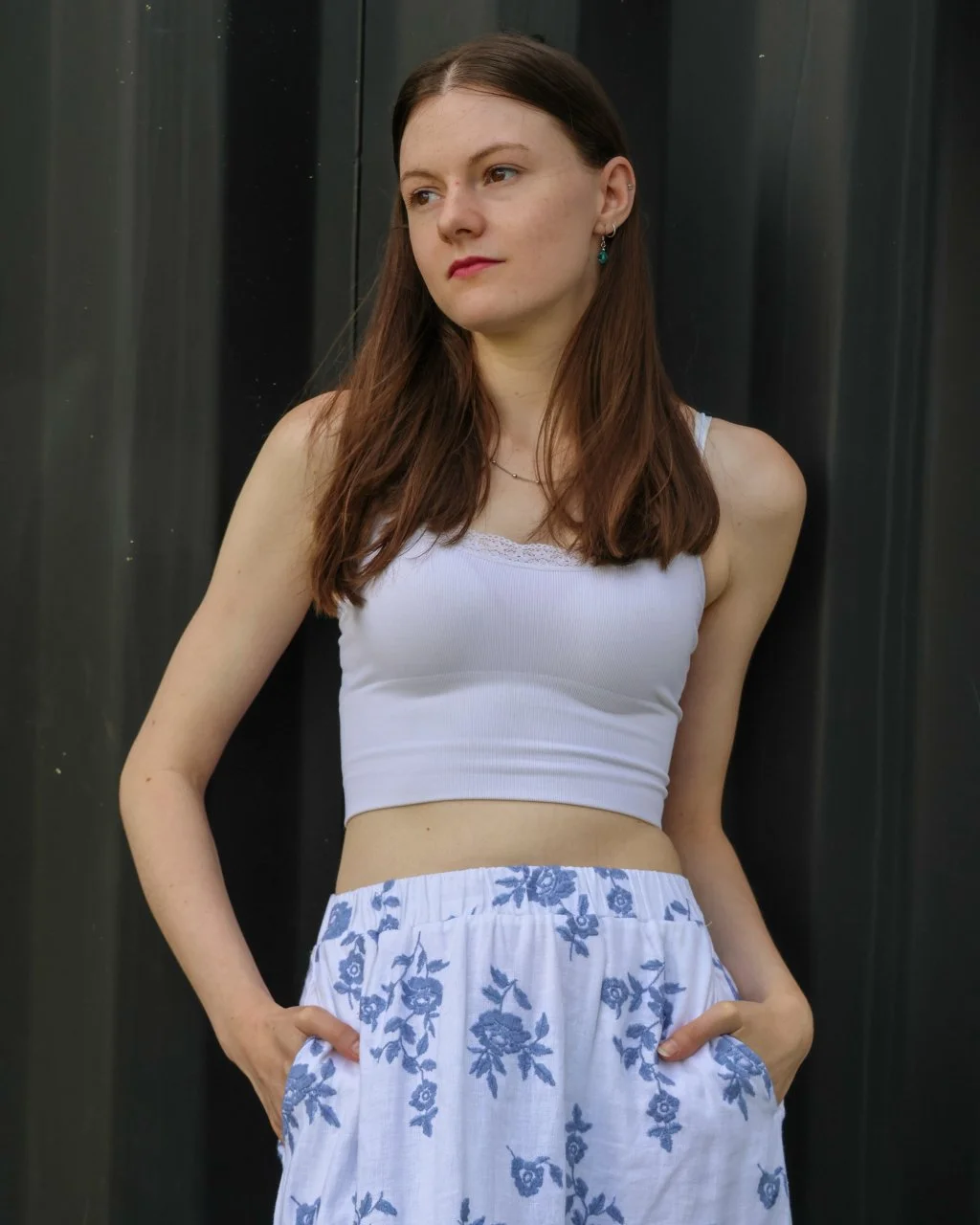 A young woman with long brown hair, brown eyes, and light complexion wearing silver earrings and a black top, looking directly at the camera against a neutral background.