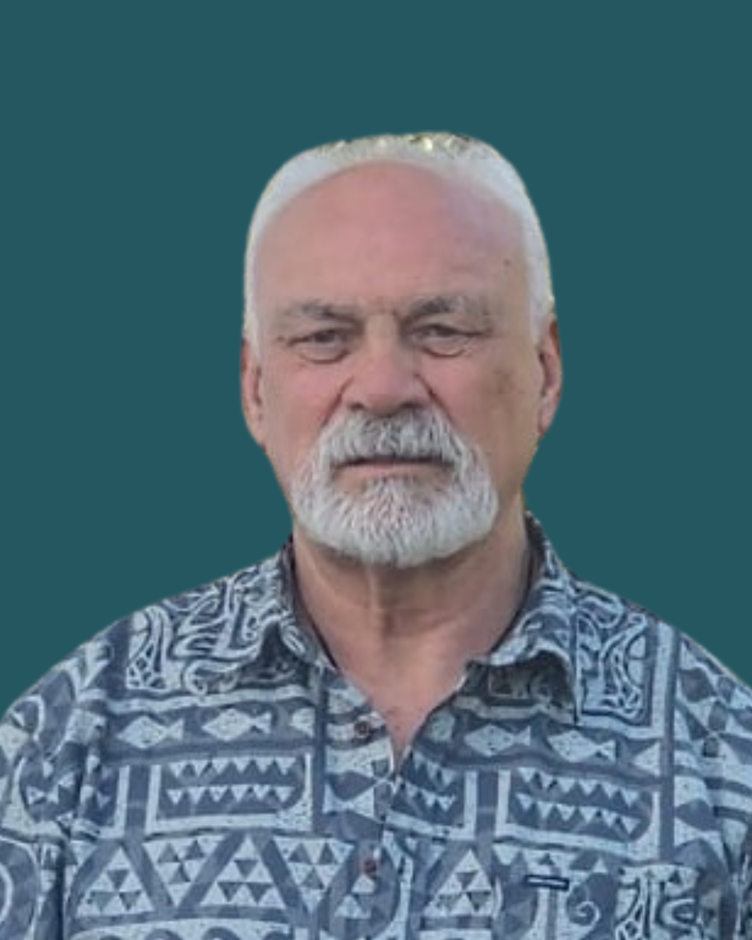 Portrait of an older man with white hair and beard, wearing a patterned shirt, against a plain teal background.
