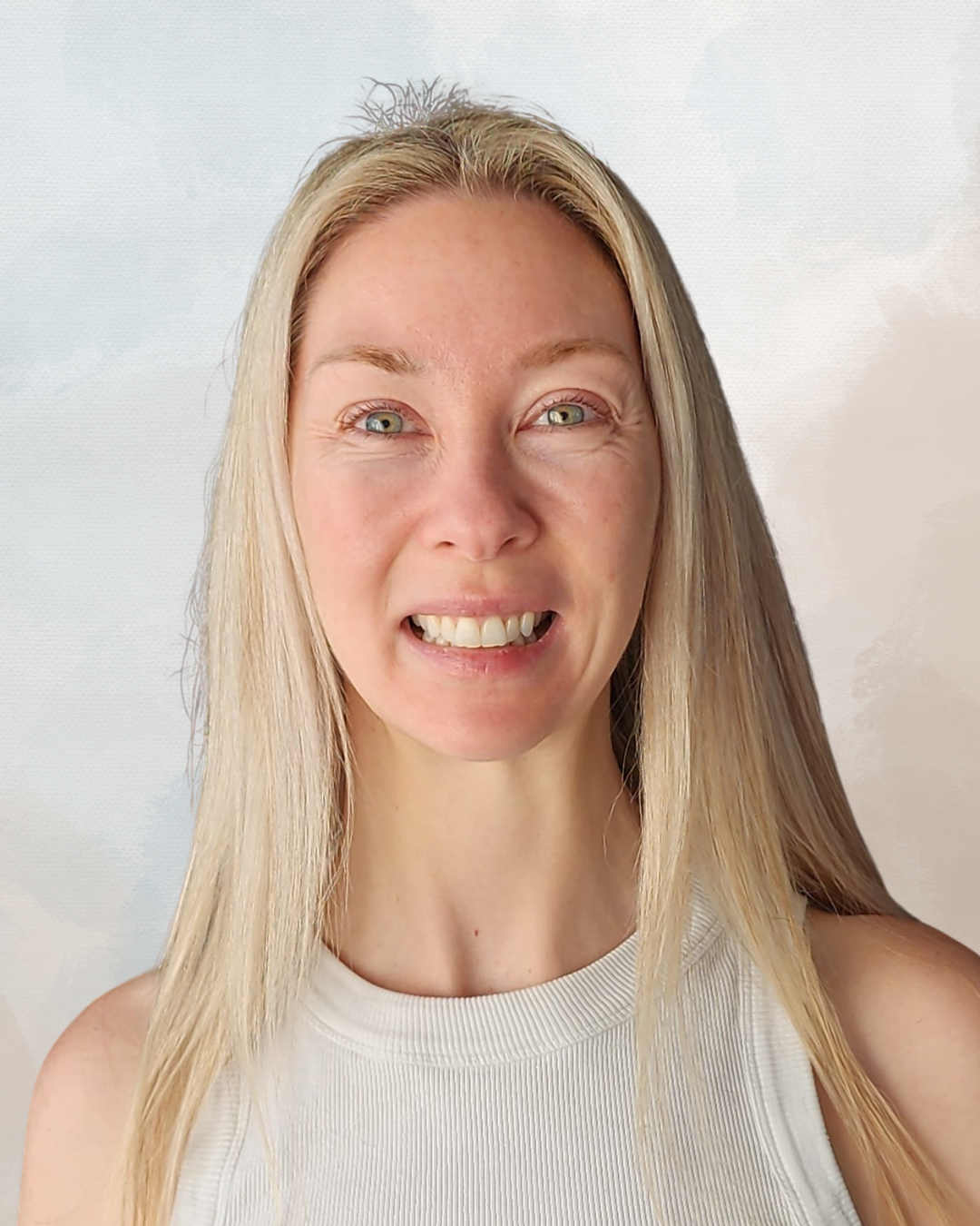 Close-up of a woman with long blonde hair, blue eyes, and a white sleeveless top, smiling and showing her teeth.
