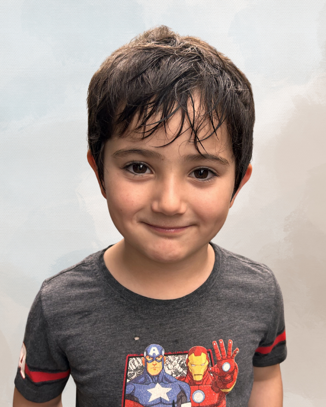 A young boy with wet, dark hair and light skin facing camera, wearing a gray T-shirt with Marvel superhero characters Captain America and Iron Man on it.