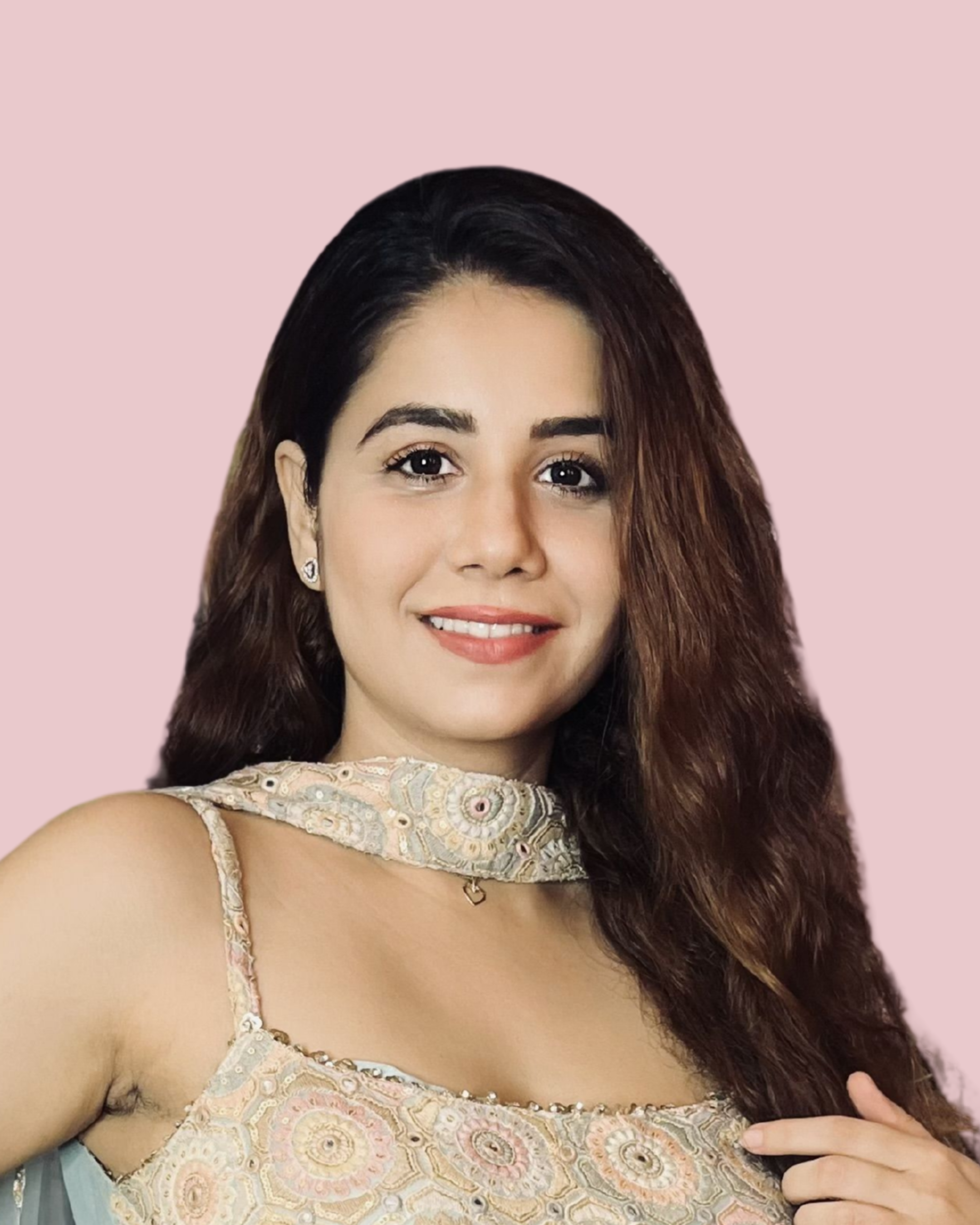 Portrait of a smiling woman with long brown hair, wearing a embroidered sleeveless dress and jewelry, standing against a pink background.