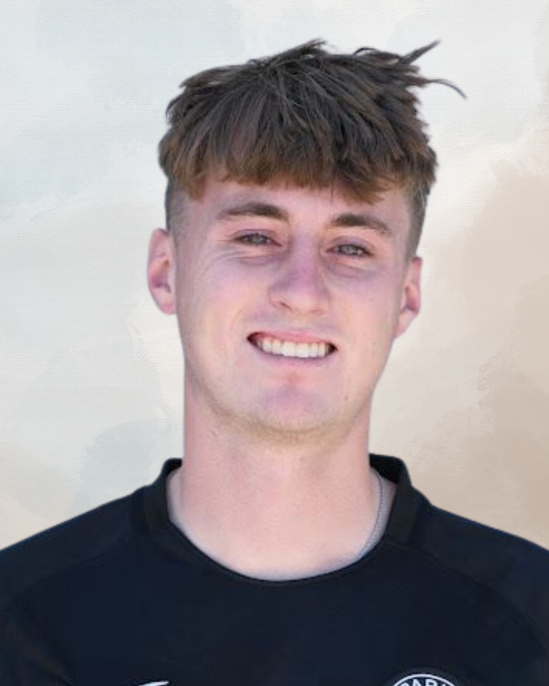 A young man with light brown hair and blue eyes smiling, wearing a black sports shirt, standing against a light background.