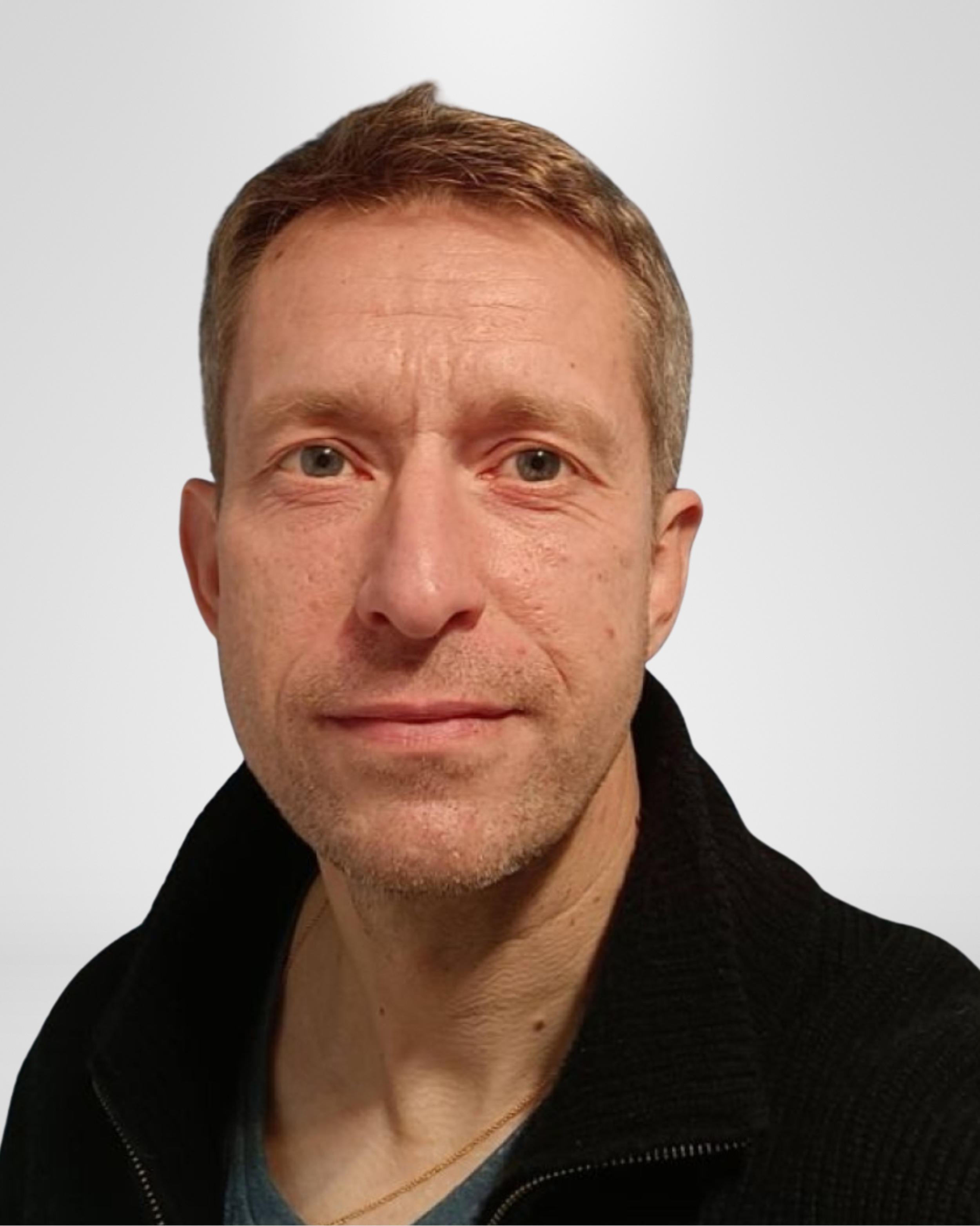 Portrait of a middle-aged man with short brown hair, blue eyes, and light skin, wearing a black jacket over a gray shirt.