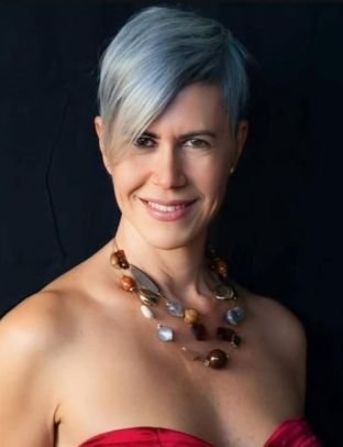 Woman with short, silver-blue hair smiling, wearing a red strapless top and a chunky necklace.